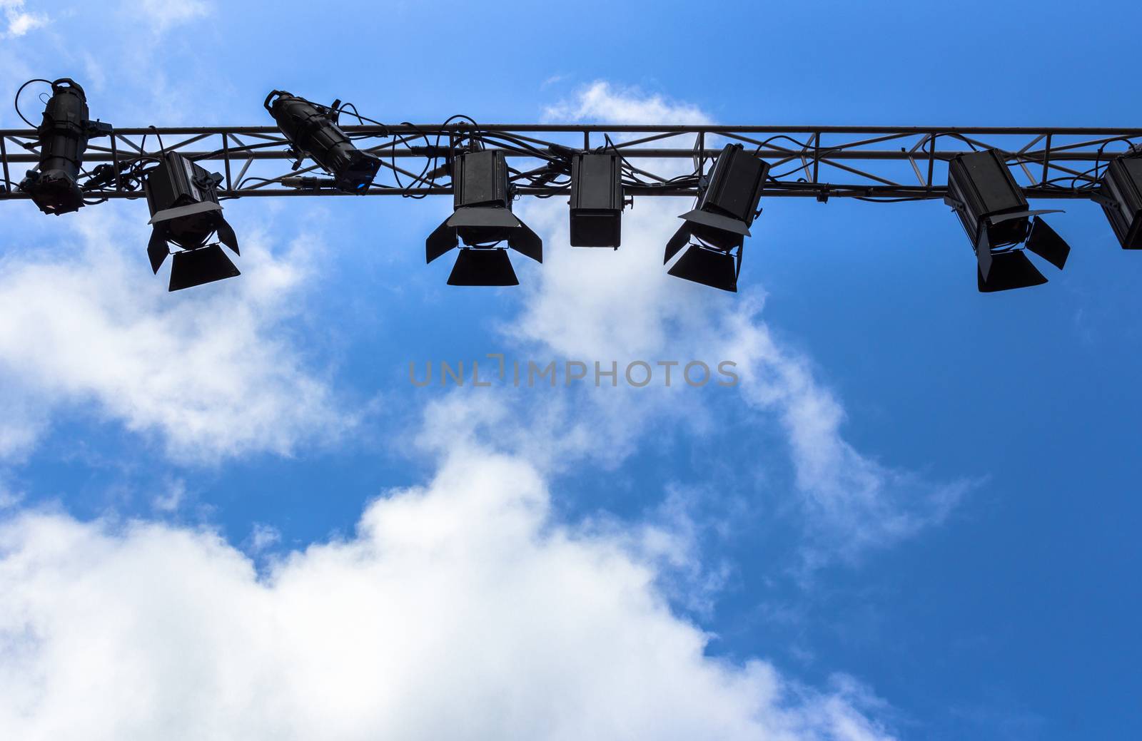 Spotlights for outdoor stage on the metal construction against a blue sky and clouds. Space for text.