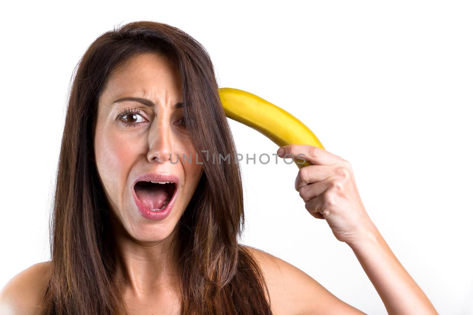 A funny portrait of a beautiful girl trying to shoot herself with a banana gun, while screaming. Cute girl having fun over white background. Space for text