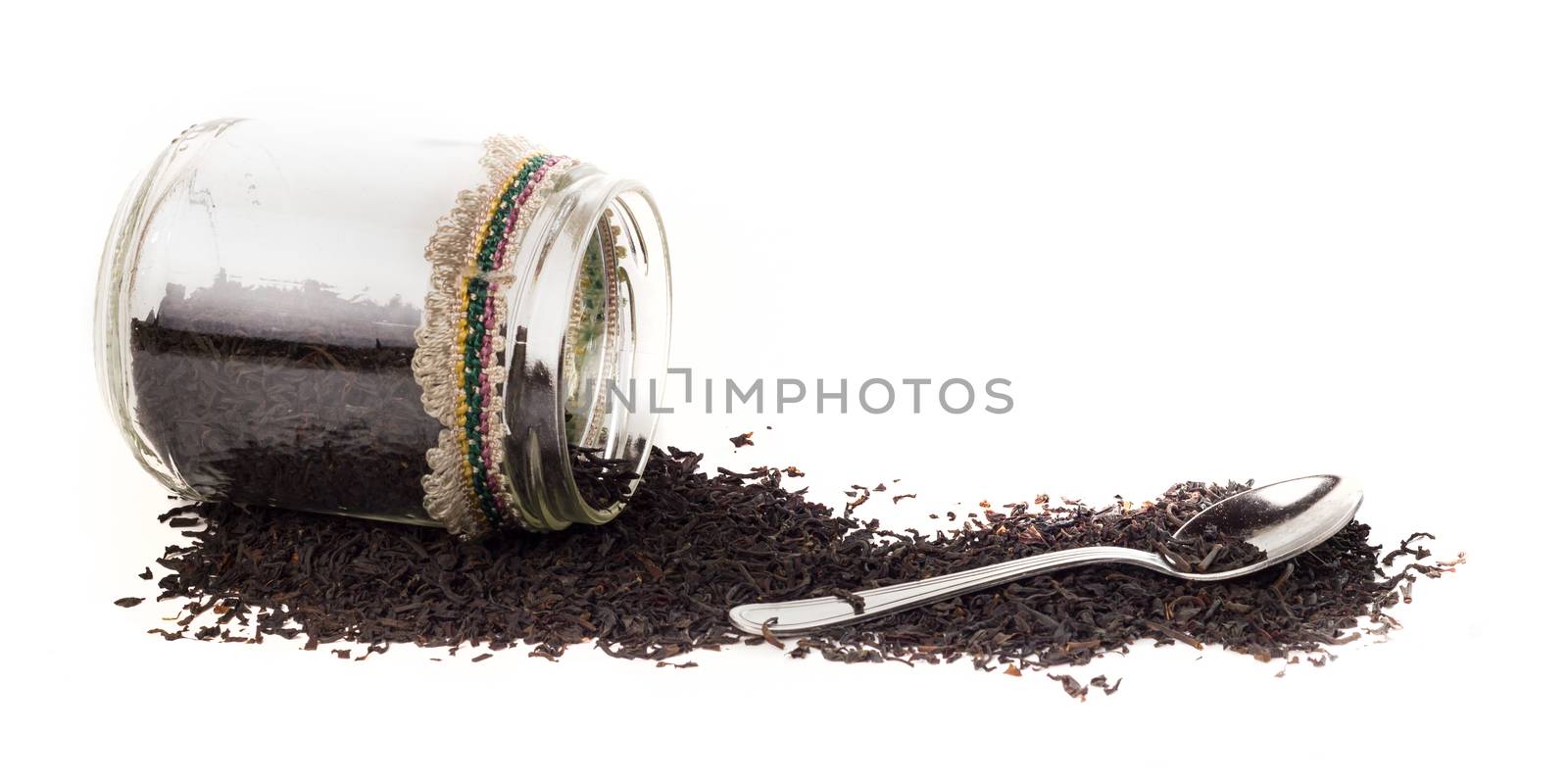 Isolated glass jar with fermented big leaves of ceylon tea on white background. On the side there is also a teaspoon