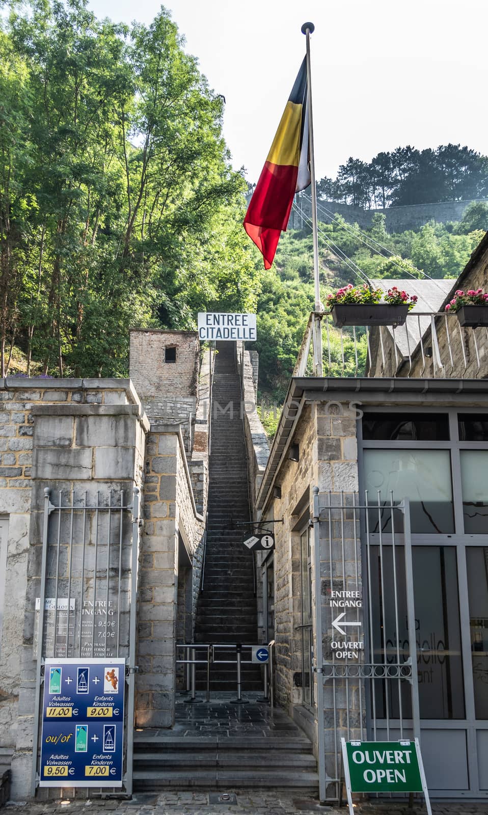 Dinant, Belgium - June 26, 2019: Entrance to the long naroow brown stone stairway up to the citadel, captured in green foliage and Belgian flag in front.