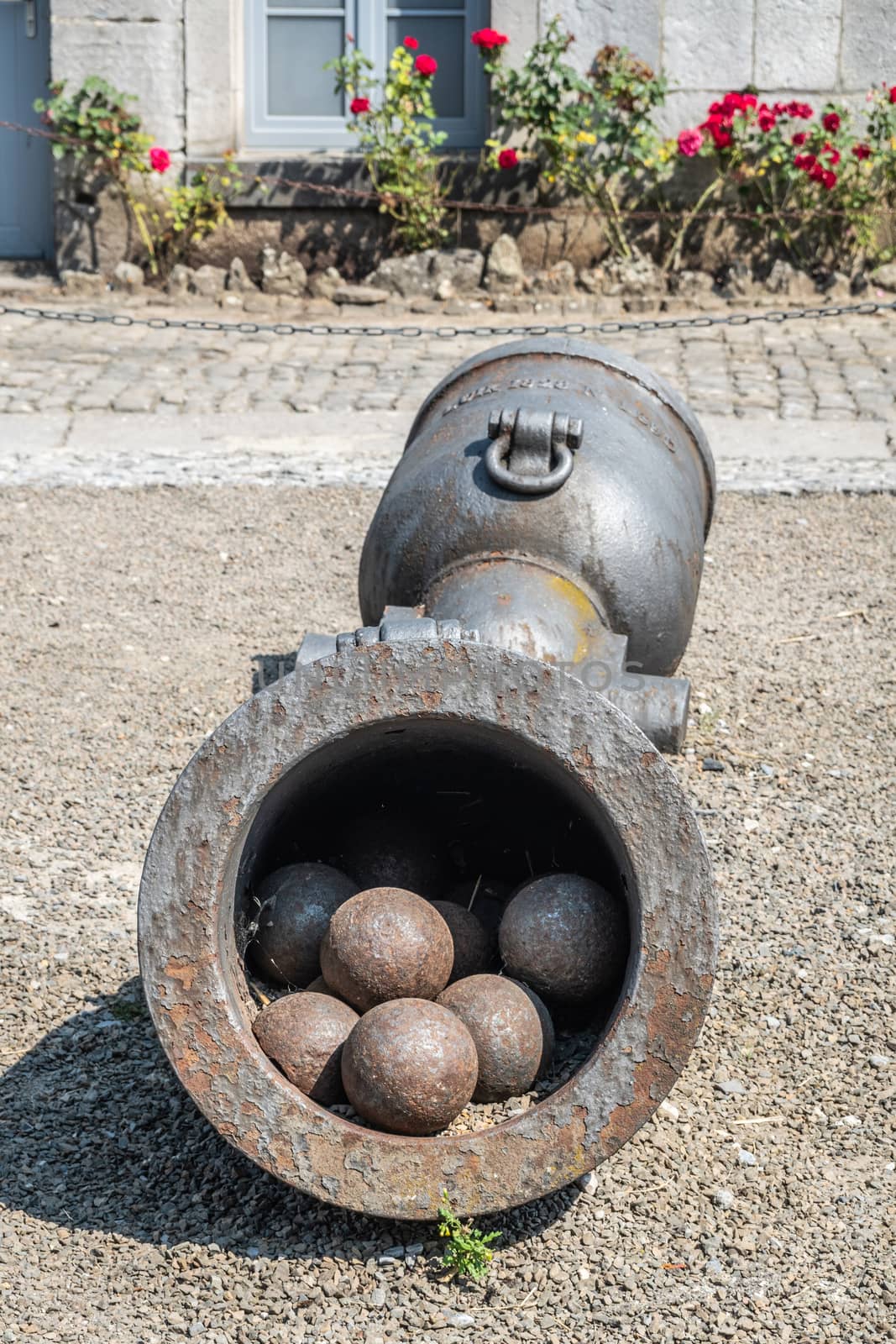 Dinant, Belgium - June 26, 2019: Seen insde Citadelle.  Closeup of Two artillery pieces, one filled with cannon balls, standing on central courtyard. Red roses in back.