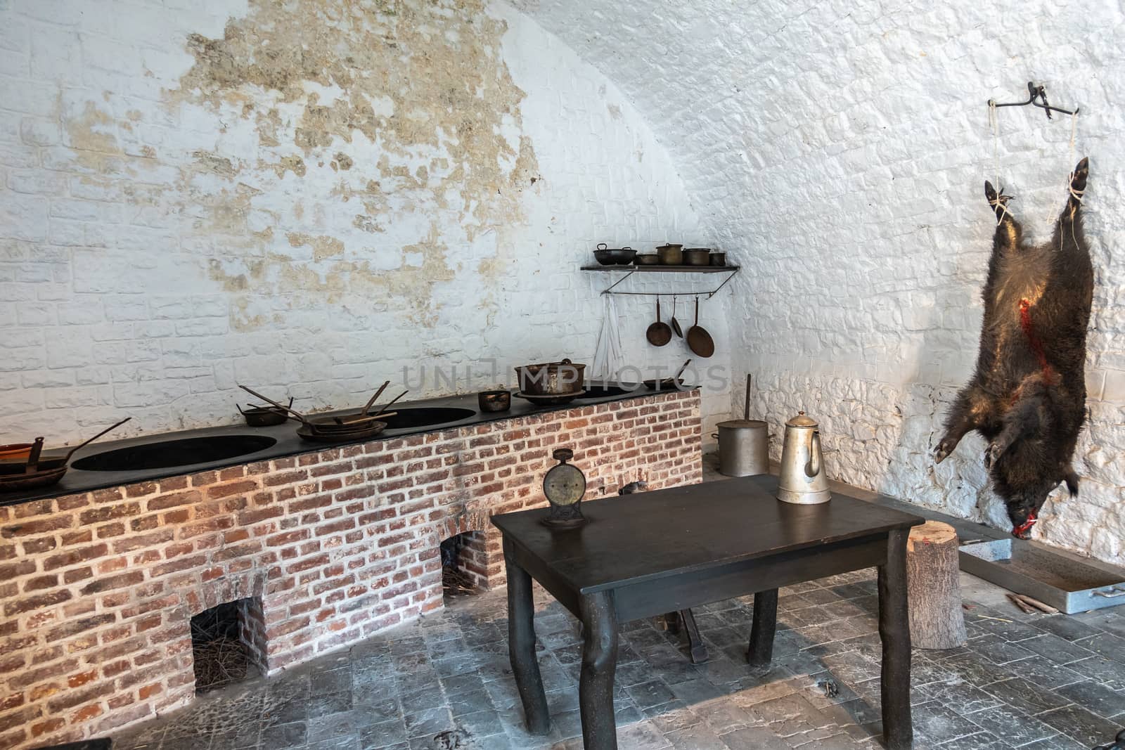 Dinant, Belgium - June 26, 2019: Inside Citadelle. Part of historic army kitchen with battery of stoves, pots and pans, and a killed boar hanging on the white pained wall.