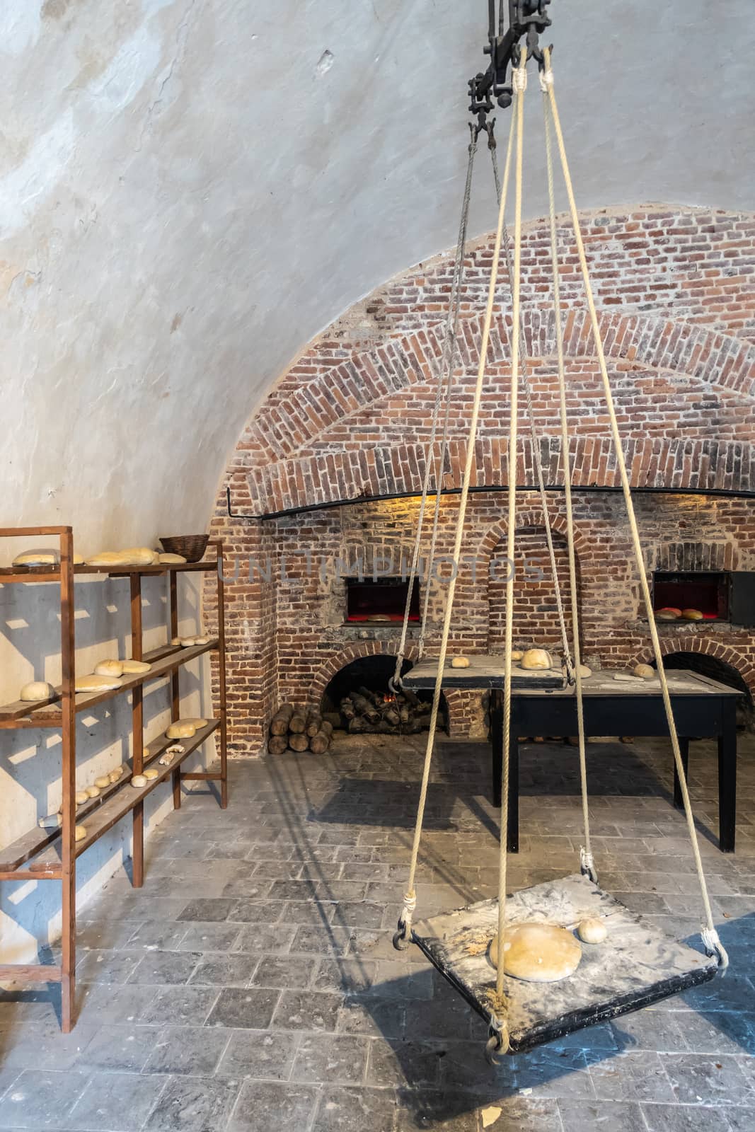Dinant, Belgium - June 26, 2019: Inside Citadelle. Part of historic bakery with shelves of bread, several open brick stone ovens, and a giant balance to weigh dough. White walls and ceililng.