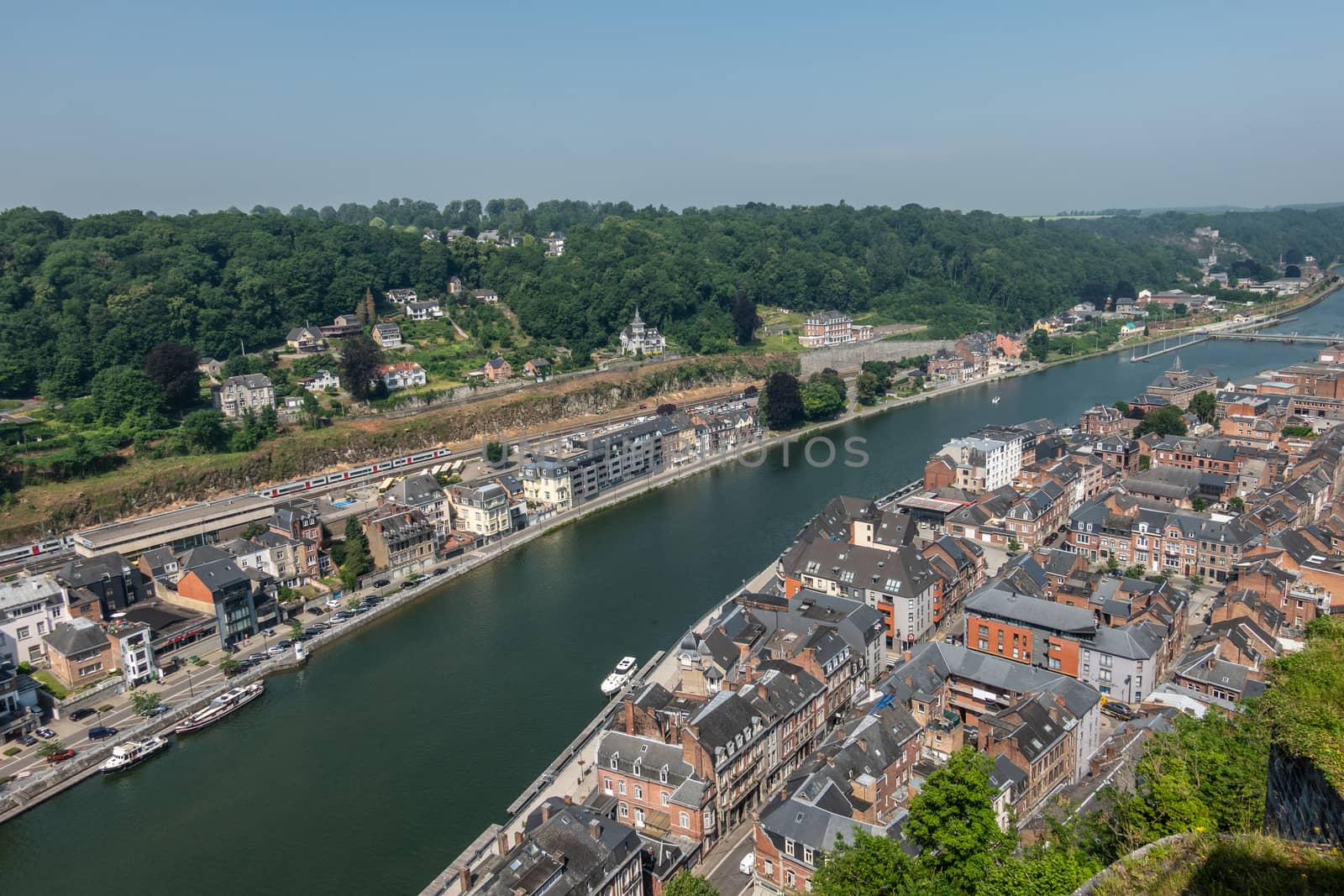 Dinant, Belgium - June 26, 2019: Seen from Citadelle. Focus on south flow of River Meuse. Green landscape, blue sky and plenty of buildings,