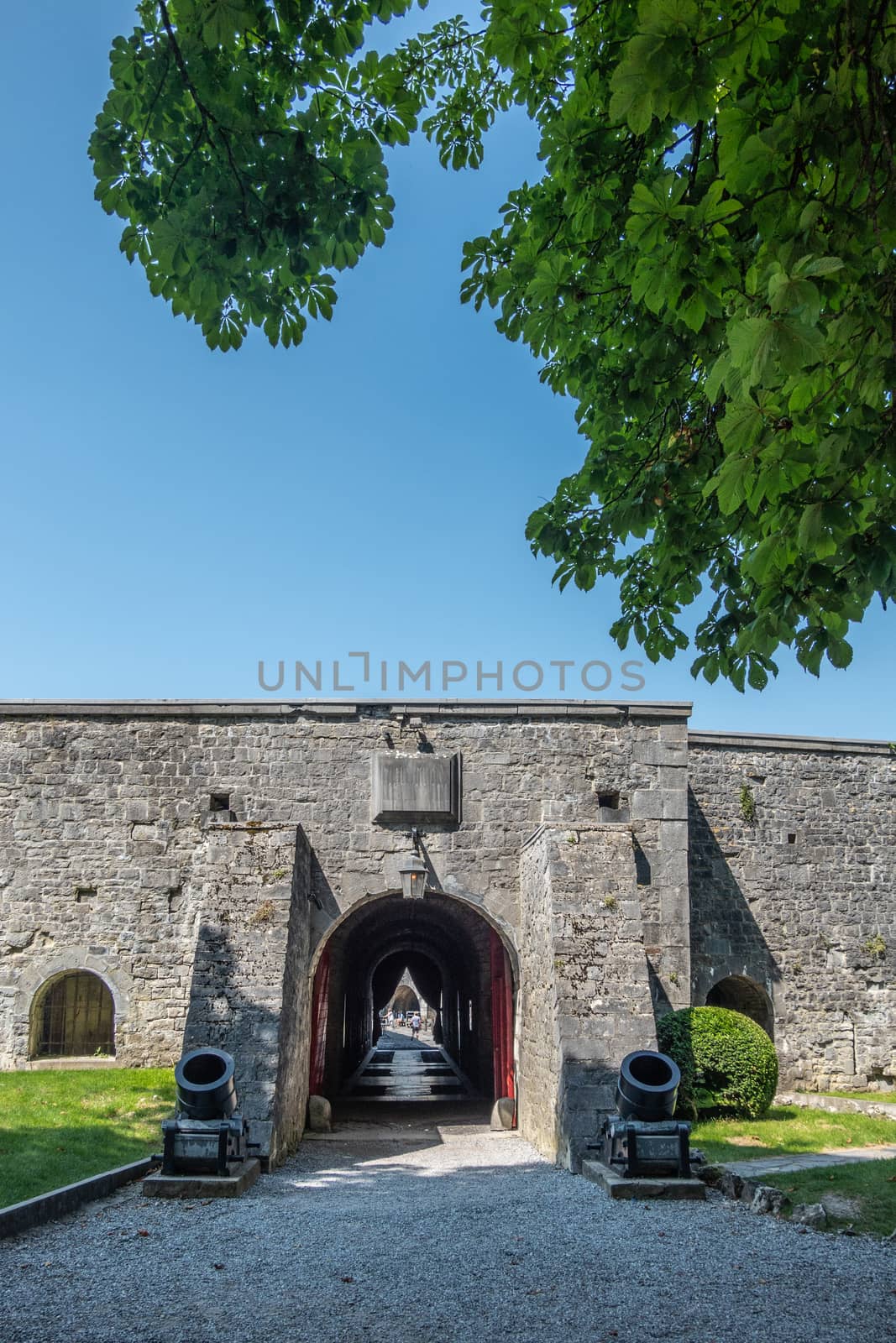 Dinant, Belgium - June 26, 2019: Inside Citadelle. Gray stoen Ramparts and gate to inner courtyard with rooms against blue sky, Green foliage.