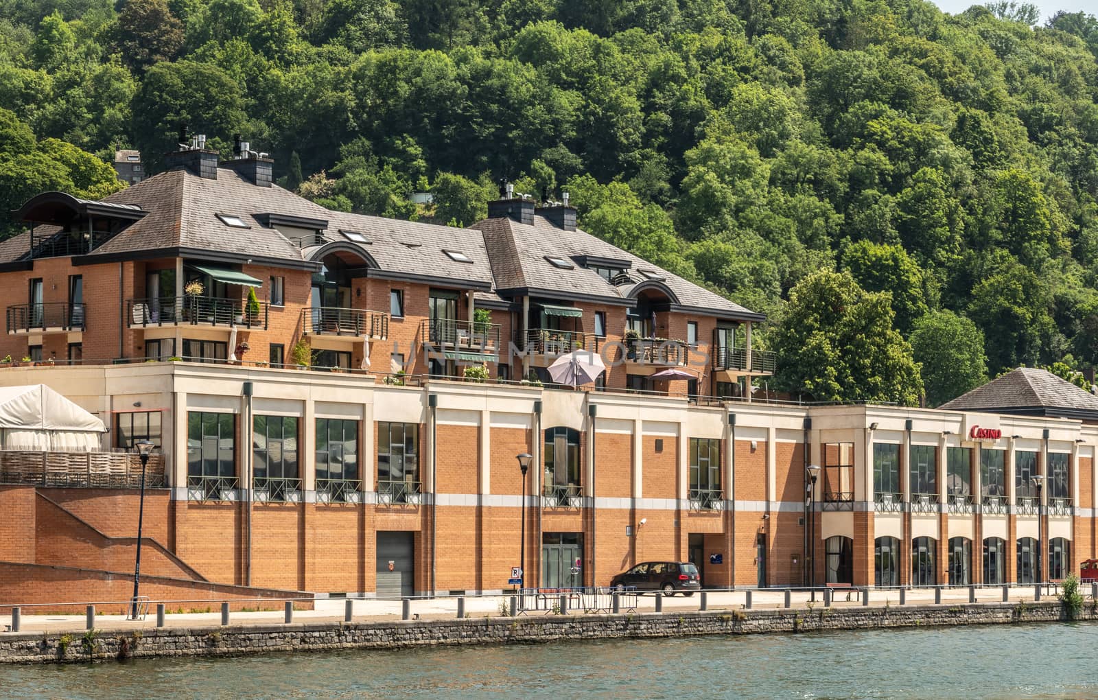 Dinant, Belgium - June 26, 2019: Beige and red stone building of the Casino and hotel along Meuse River backed by green foliage.