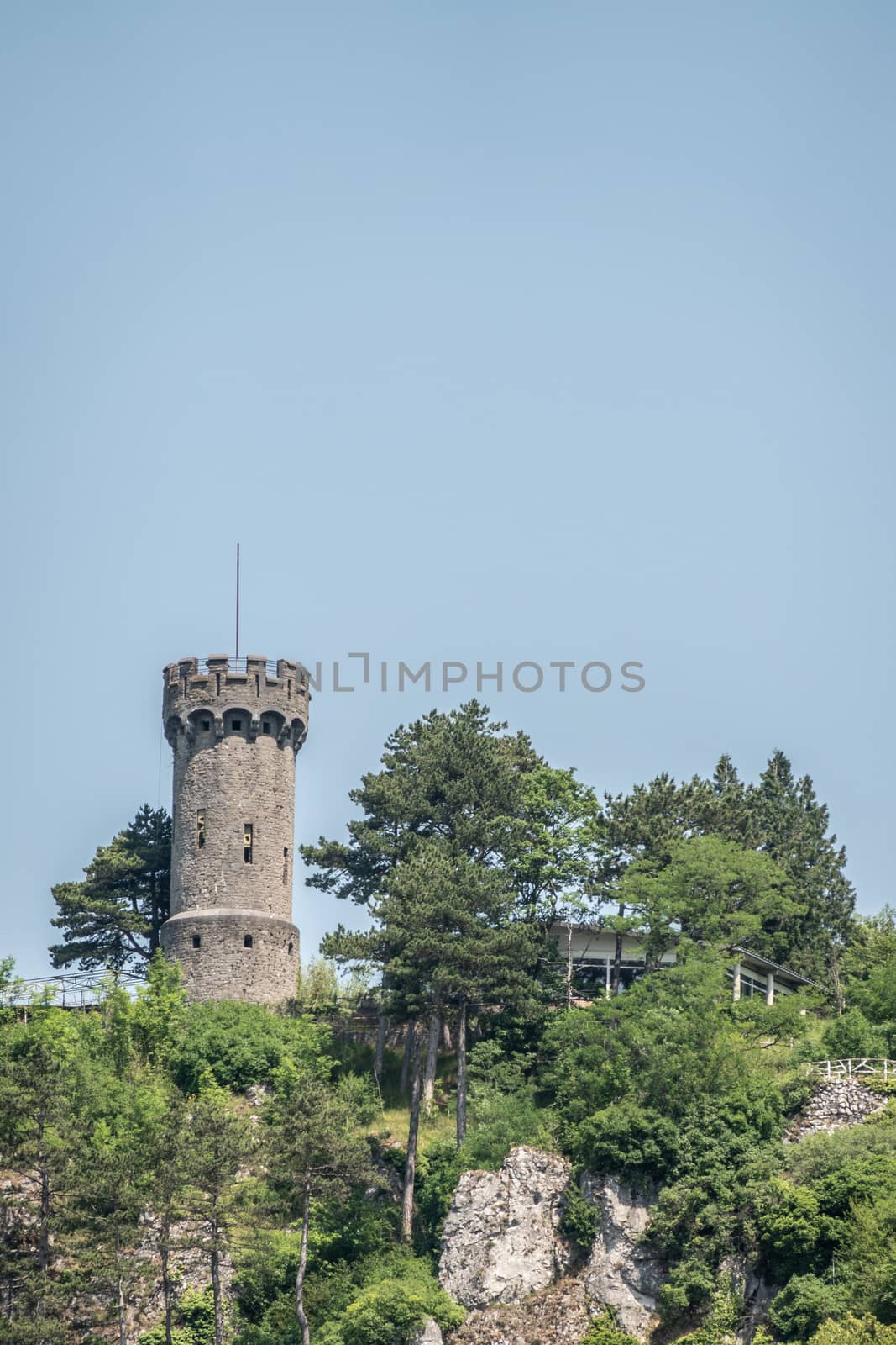 Dinant, Belgium - June 26, 2019: Brown stone watch tower of Citadelle fortification under blue sky on top of rocks and surrounded by green foliage.