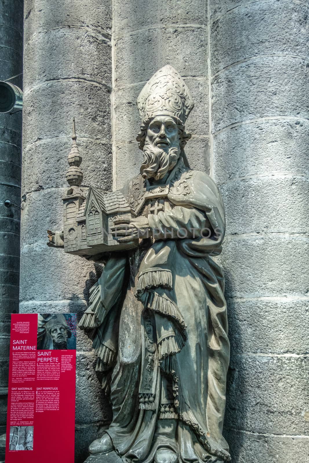 Dinant, Belgium - June 26, 2019: Inside Collégiale Notre Dame de Dinant Church. Gray stone statue of Belgian medieval Saint Materne against pillar. Red sign with history.