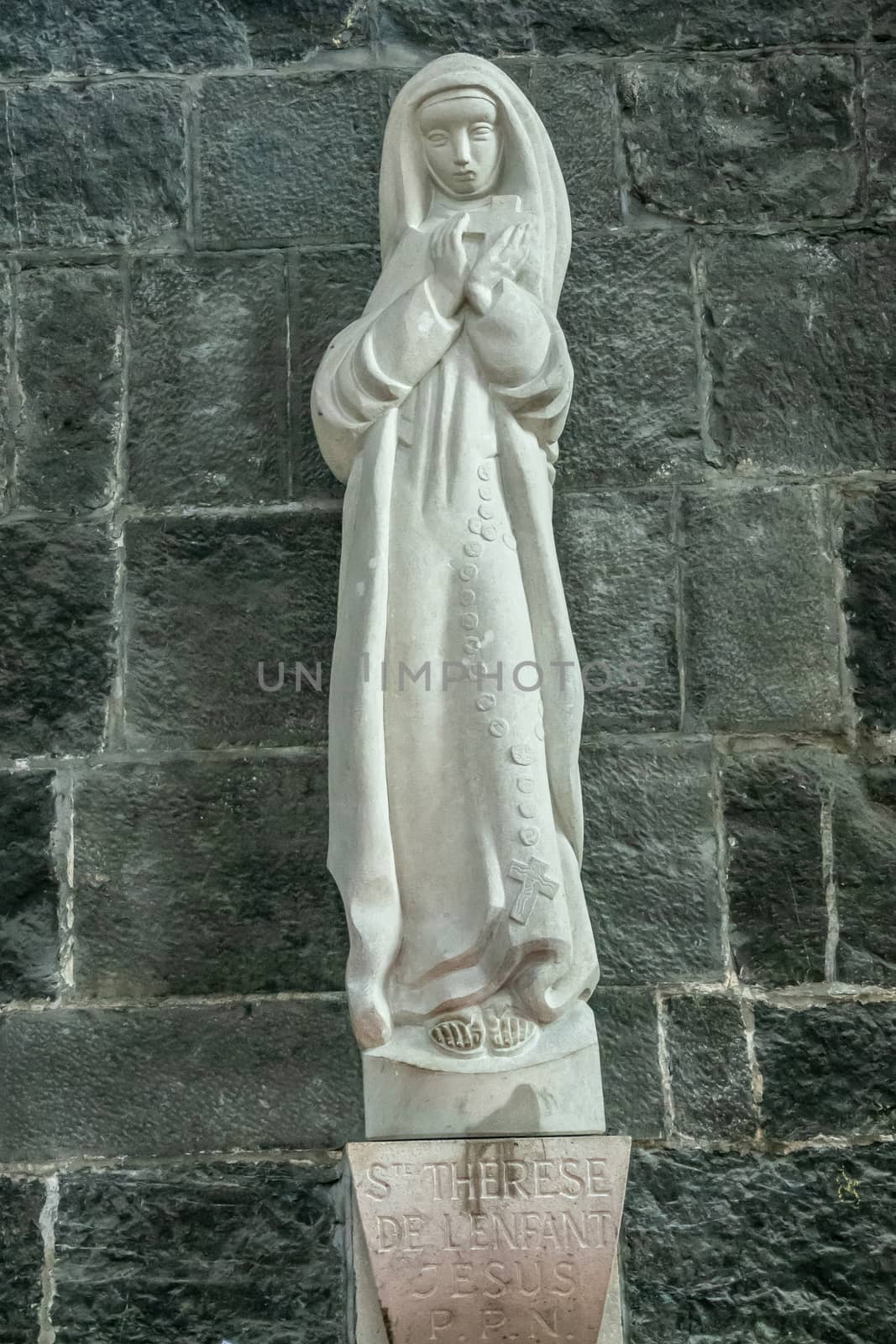 Dinant, Belgium - June 26, 2019: Inside Collégiale Notre Dame de Dinant Church. Modern style white stone statue of Sainte Therese of the child Jesus against gray stone church wall.