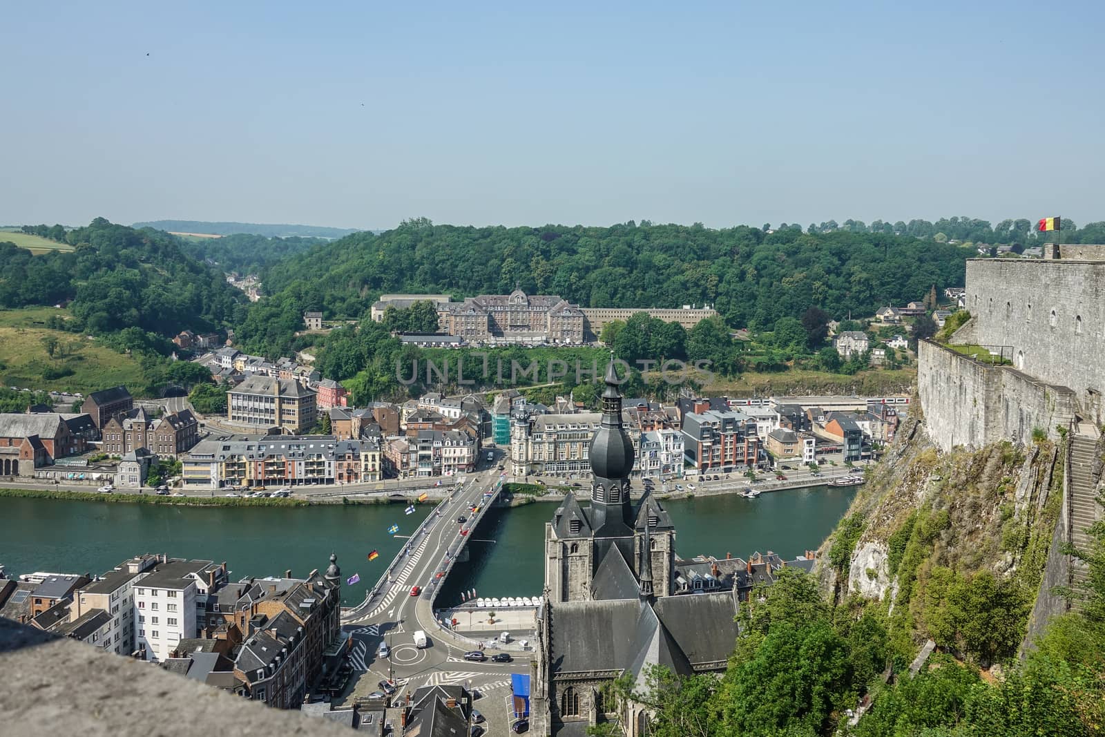 Dinant, Belgium - June 26, 2019: Seen from Citadelle. Large building on top is College Notre Dame de Bellevue, school system from primary to high school. Forests in back. Church and ramparts of Citadelle.