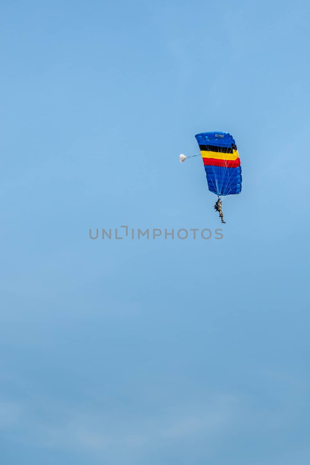 Han-sur-Lesse, Belgium - June 25, 2019: Belgian soldier on parachute with Belgian flag colors against blue sky.