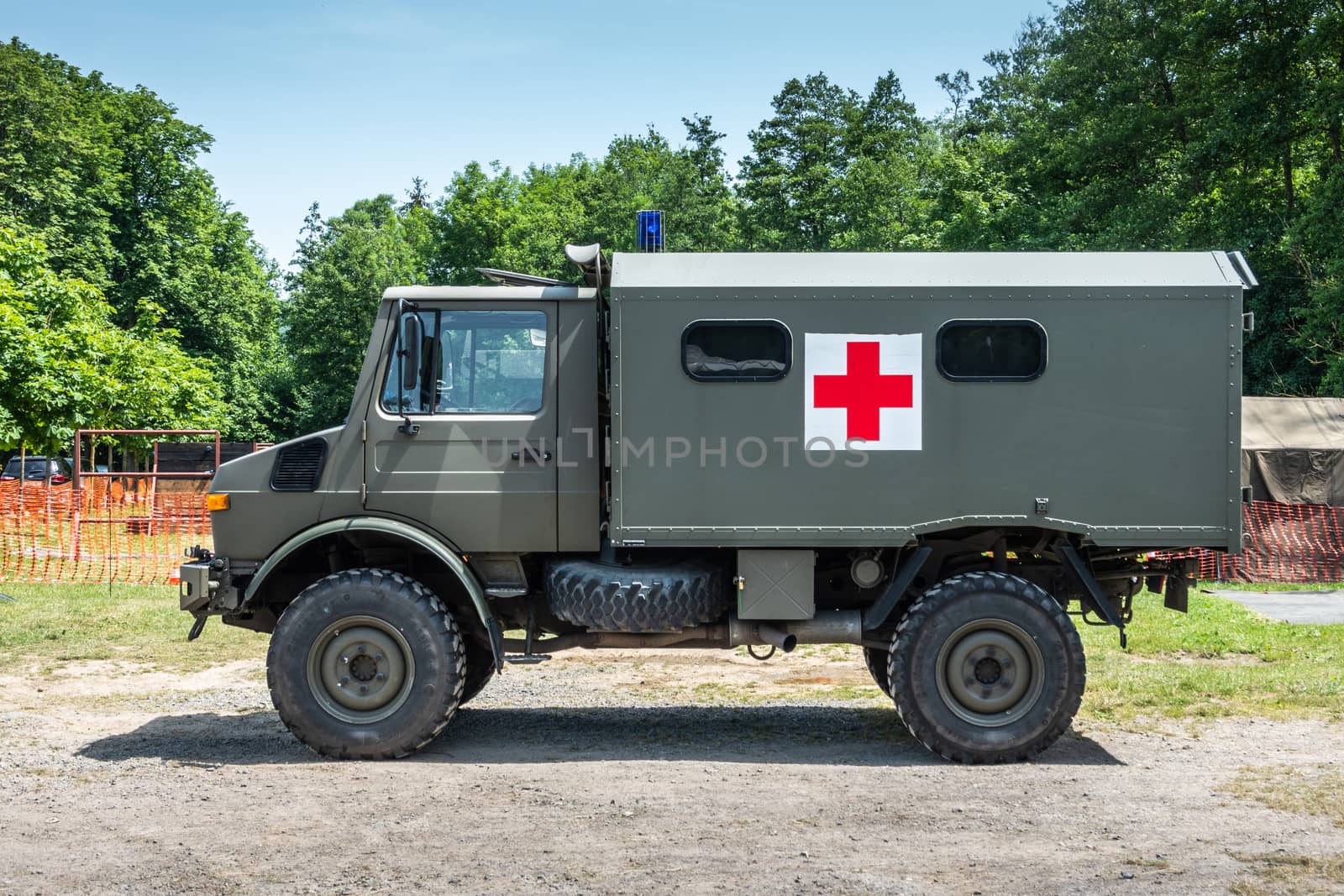 Han-sur-Lesse, Belgium - June 25, 2019: Belgian army green ambulance truck with red cross symbol against green foliage and light blue sky.
