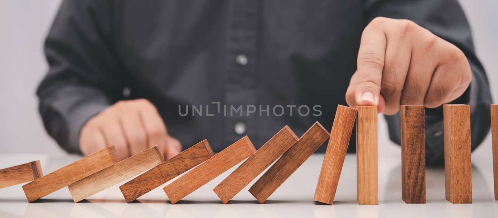 business man hand stop falling wooden stick (dominoes) . risk management in business concept.