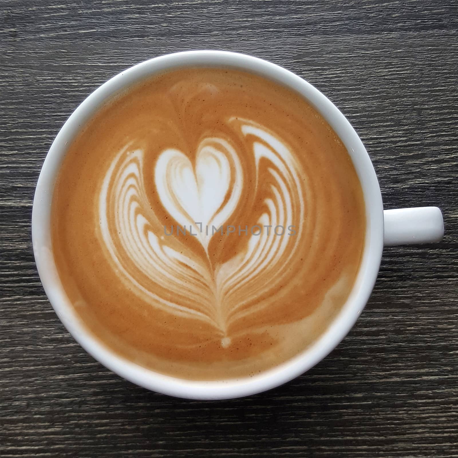 Top view of a mug of latte art coffee on timber background.