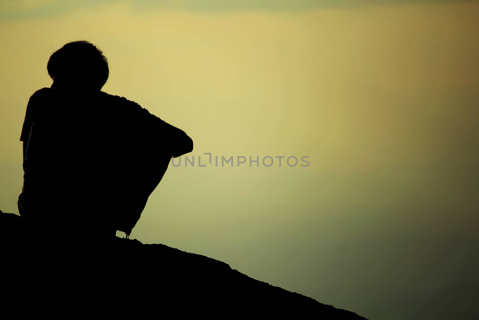 Silhouette of a boy sitting on a rock by Puripatt