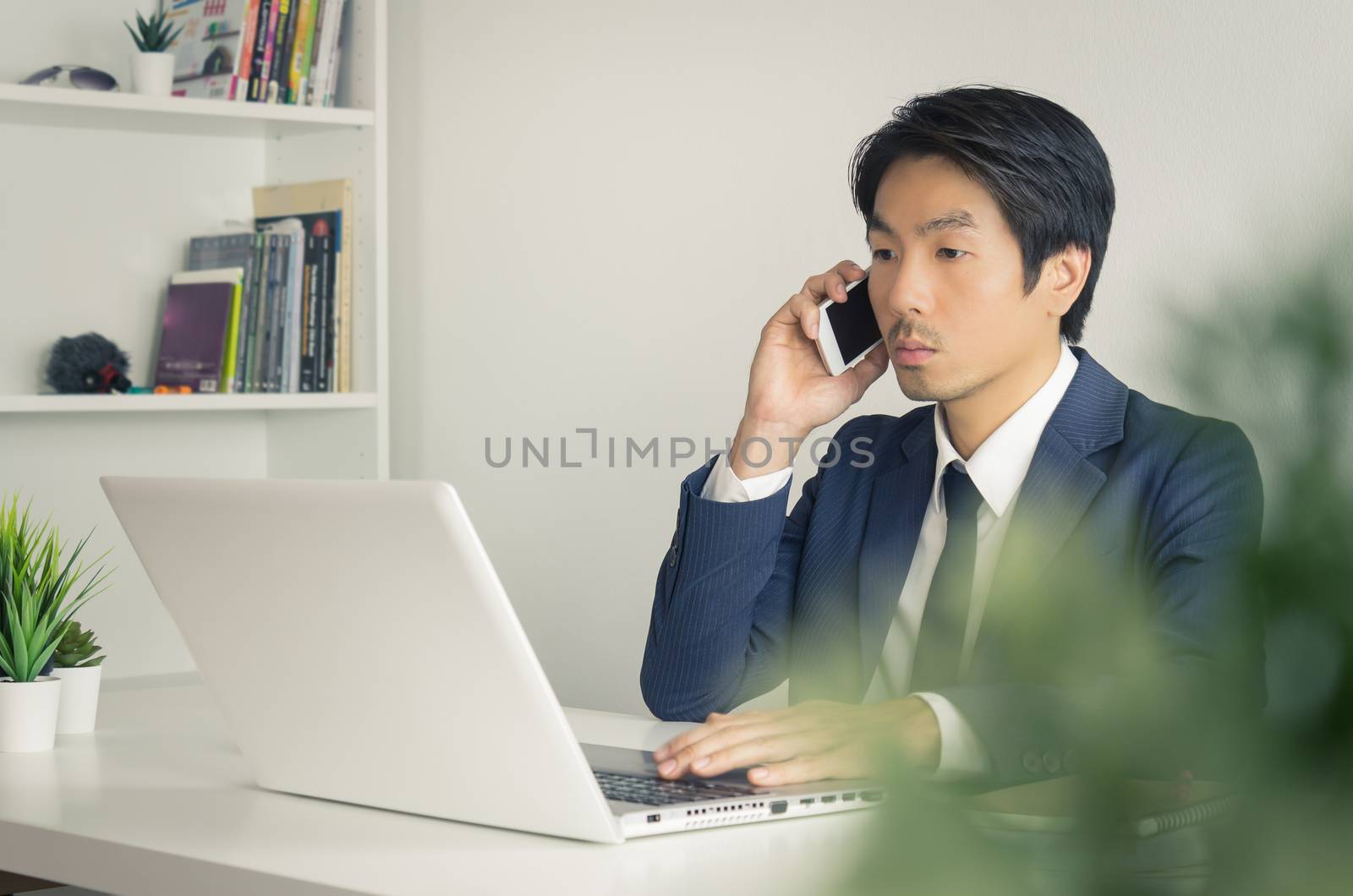 Portrait Asian Businessman in Formal Navy Blue Suit Working in Office and Using Smartphone and Laptop. Asian businessman with laptop and smartphone