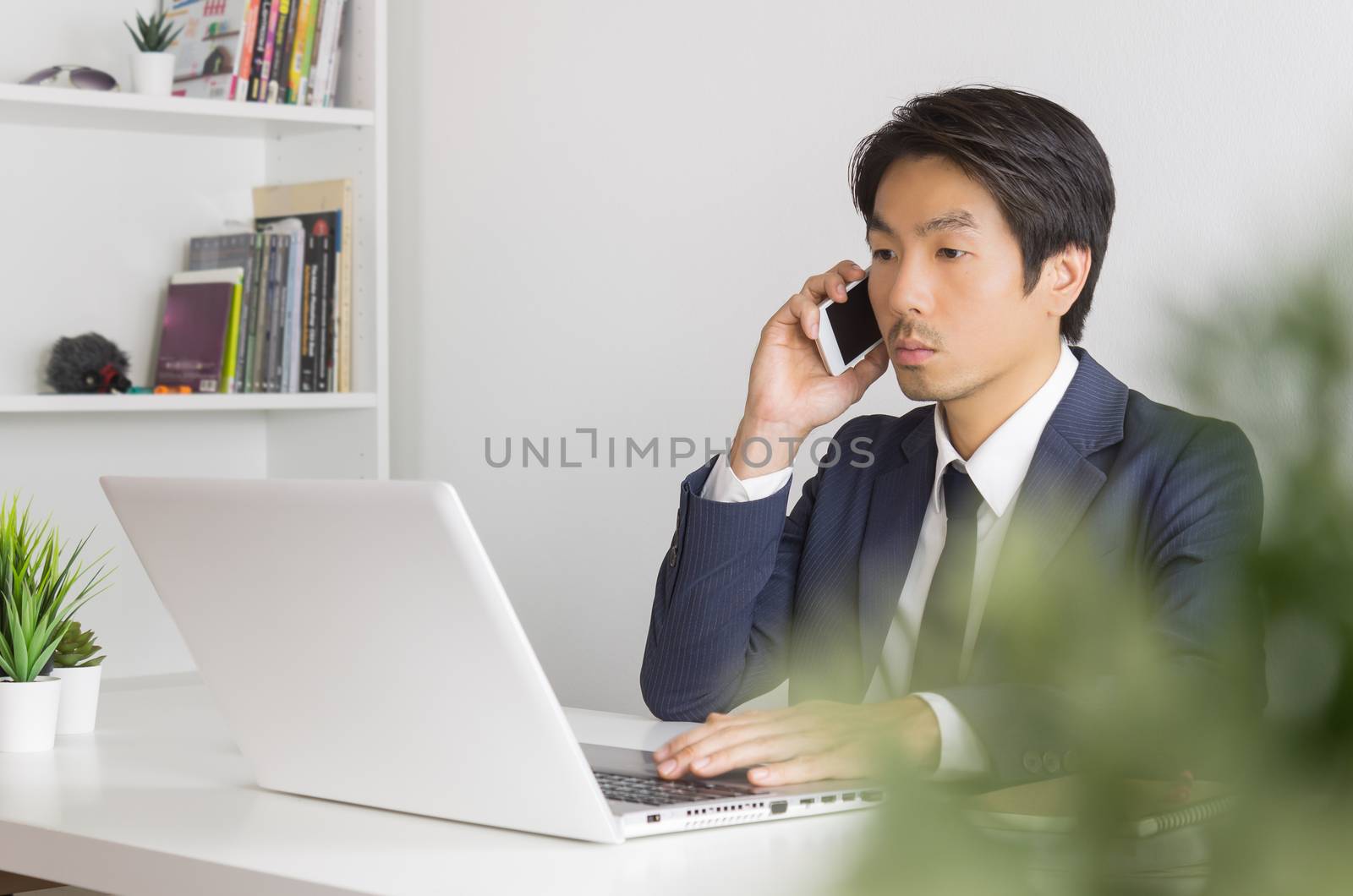 Portrait Asian Businessman in Formal Navy Blue Suit Working in Office and Using Smartphone and Laptop. Asian businessman with laptop and smartphone