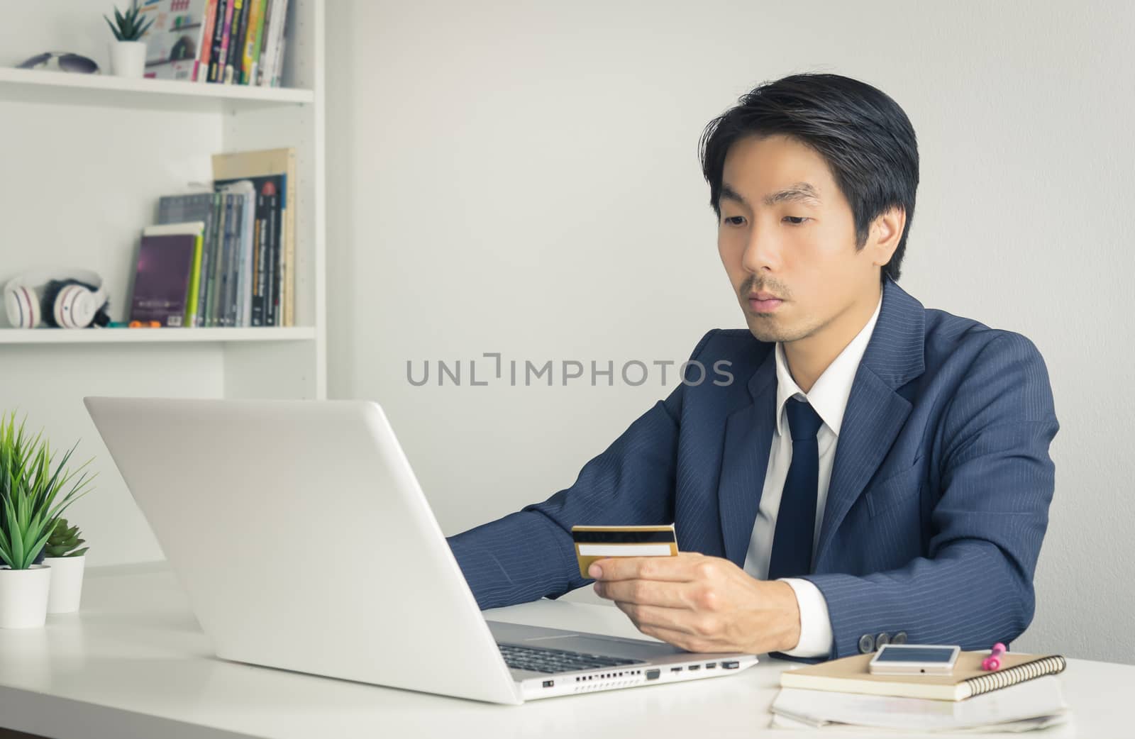 Asian Businessman in Formal Navy Blue Suit Shopping Online by Credit Card in Office. Asian businessman buying product online by credit card payment method