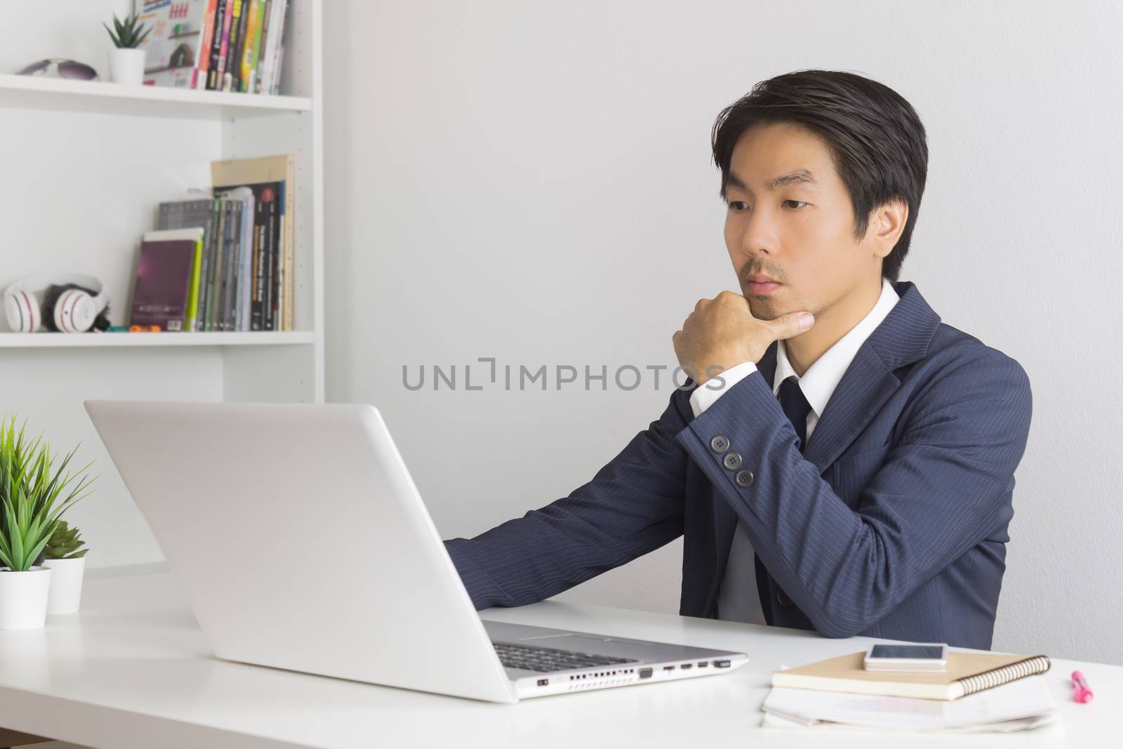 Asian Financial Advisor or Asian Consulting Businessman in Suit Thinking in front of Laptop Monitor in Office. Asian financial advisor or Asian consulting businessman contact with customer
