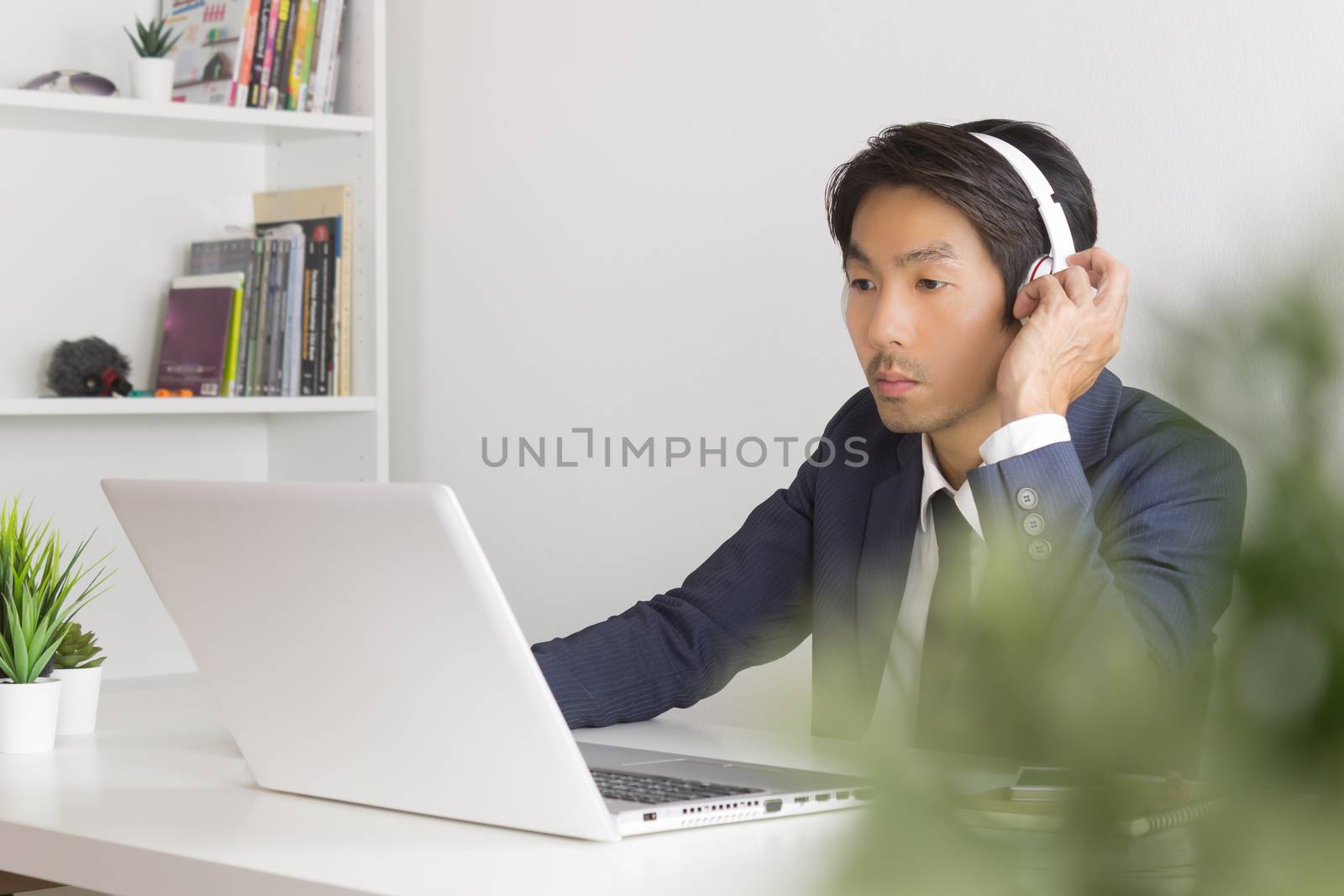 Asian Man Call Center Communicate with Customer via Internet by Laptop with Tree Foreground. Asian man call center answers the customer question in office