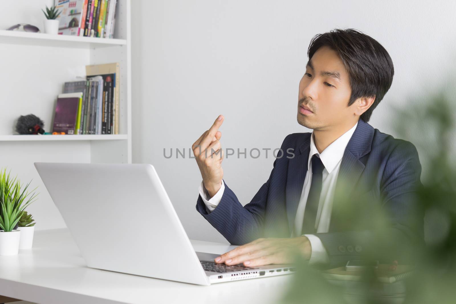 Angry Asian Businessman in Suit Show Middle Finger in front of Laptop Monitor. Agitate Asian businessman with stain with pressure condition in office
