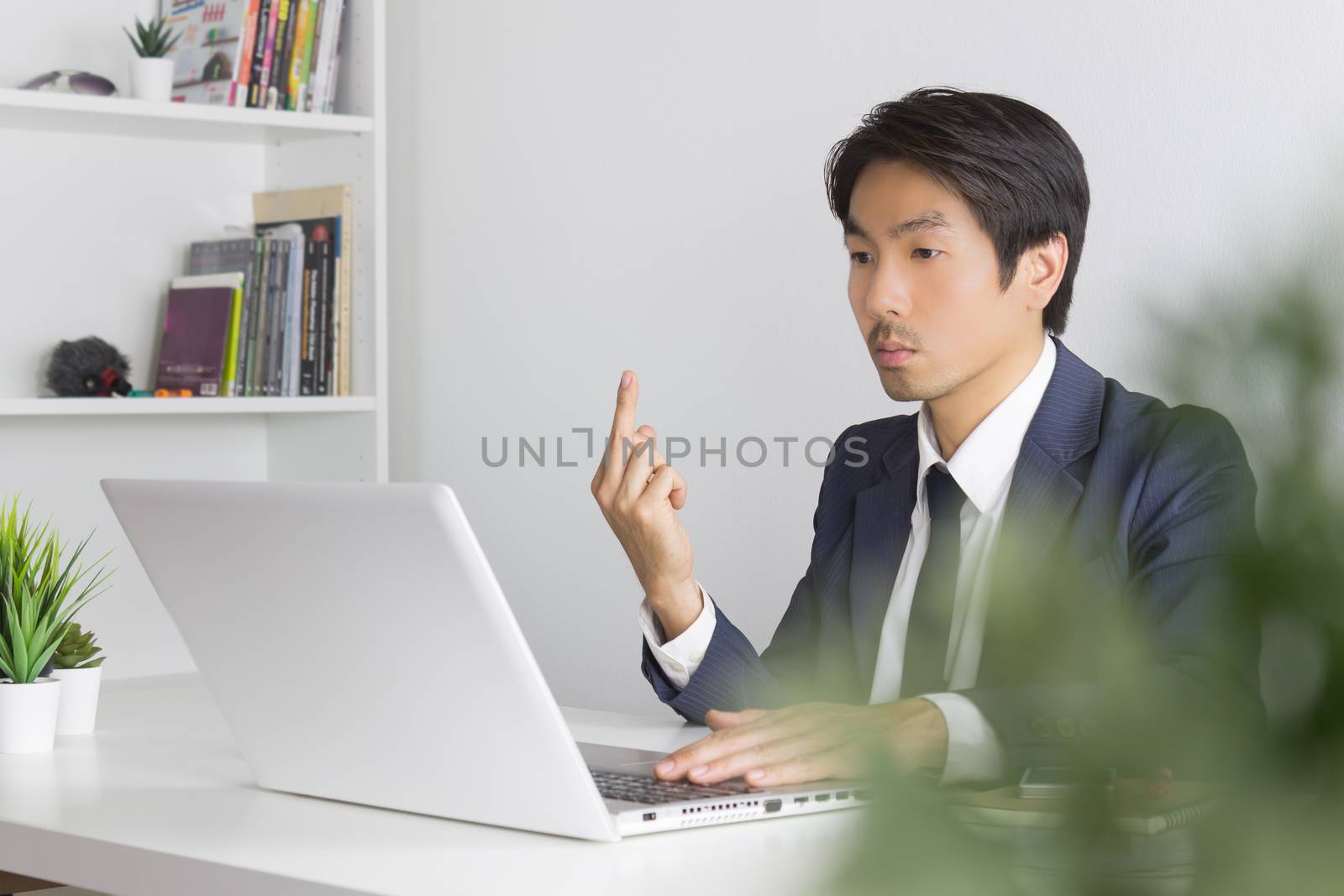 Asian Businessman Angry Partner and Show Middle Finger in front of Laptop. Vulgarity of Asian businessman in pressure condition