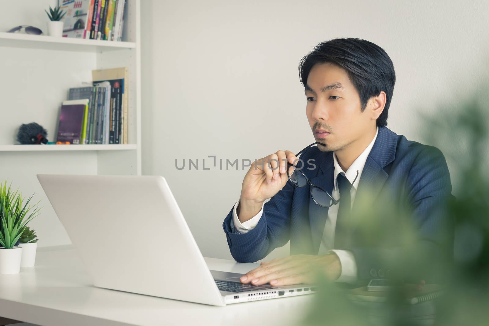Asian Financial Advisor or Asian Consulting Businessman Serious with Financial Information in front of Laptop. Asian financial advisor or Asian consulting businessman working in office