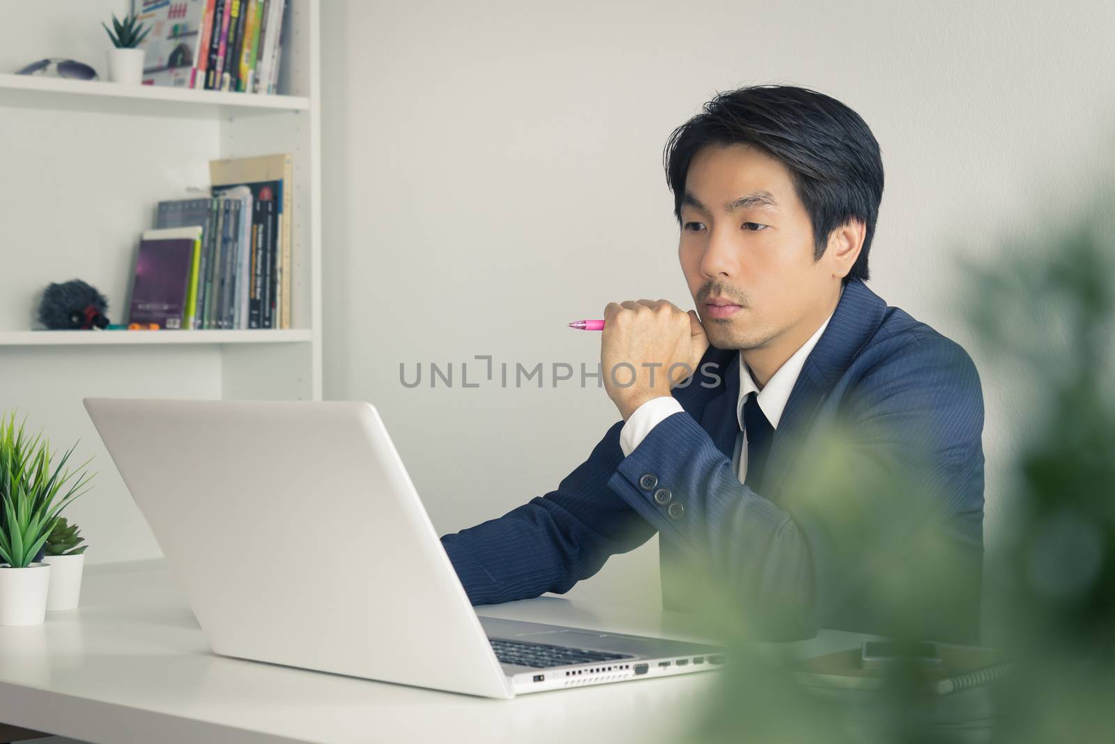 Asian Financial Advisor or Asian Consulting Businessman in Suit Seriously Thinking in front of Laptop. Asian financial advisor or Asian consulting businessman contact with customer via internet