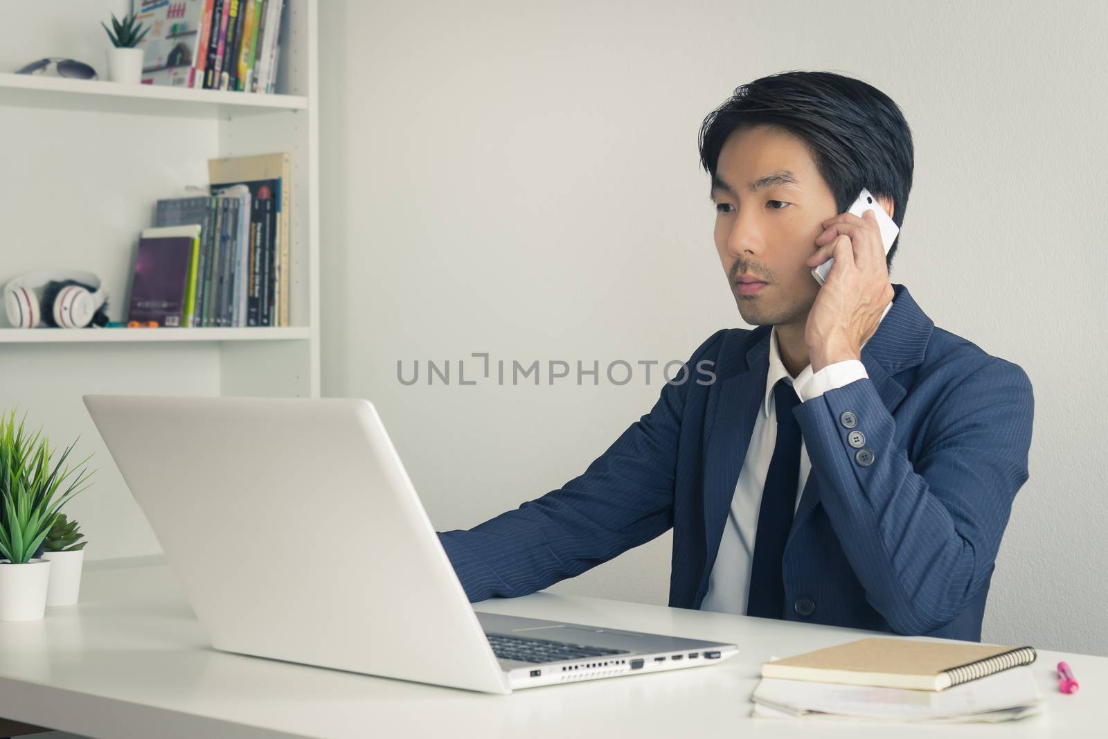 Asian Financial Advisor or Asian Consulting Businessman in Suit Talking with Customer by use Smartphone and Laptop. Asian Financial Advisor or Asian Consulting Businessman working in office