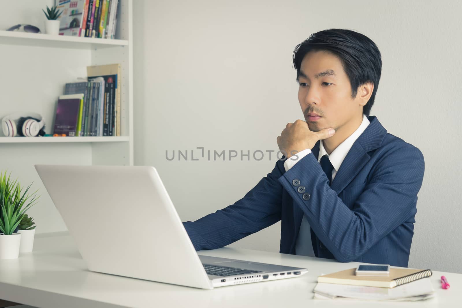 Asian Financial Advisor or Asian Consulting Businessman in Suit Thinking in front of Laptop Monitor in Office. Asian financial advisor or Asian consulting businessman contact with customer