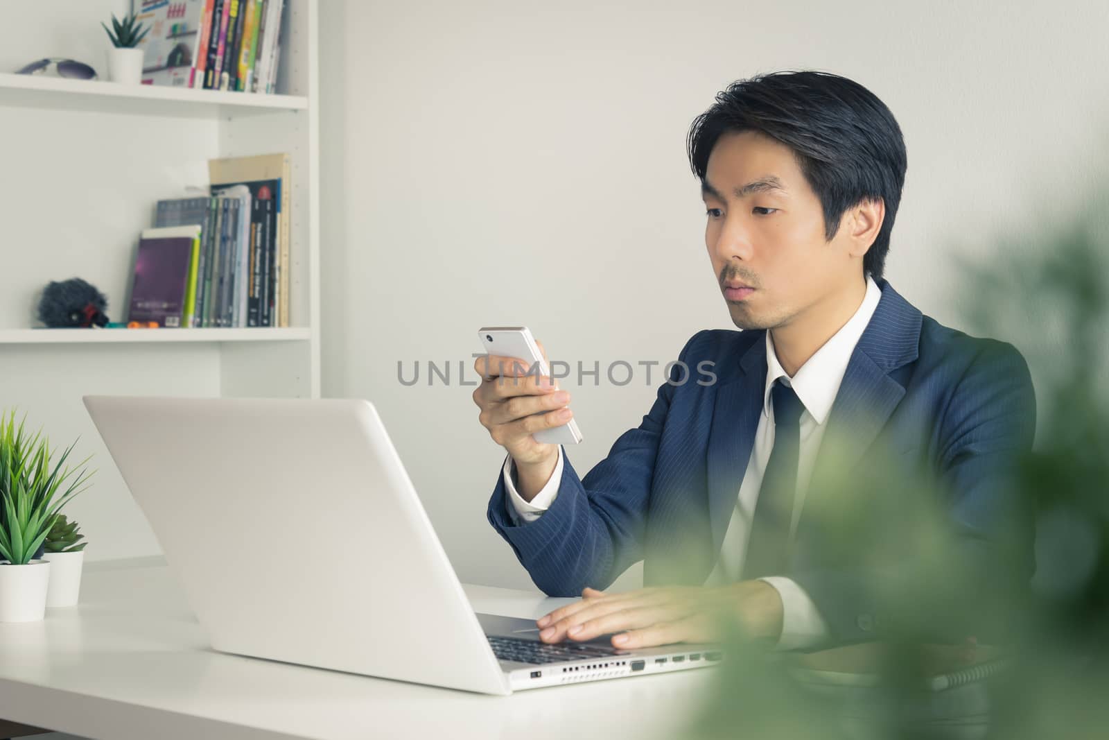 Asian Financial Advisor or Asian Consulting Businessman Use Smartphone and Laptop in Office. Asian financial advisor or Asian consulting businessman contact with customer