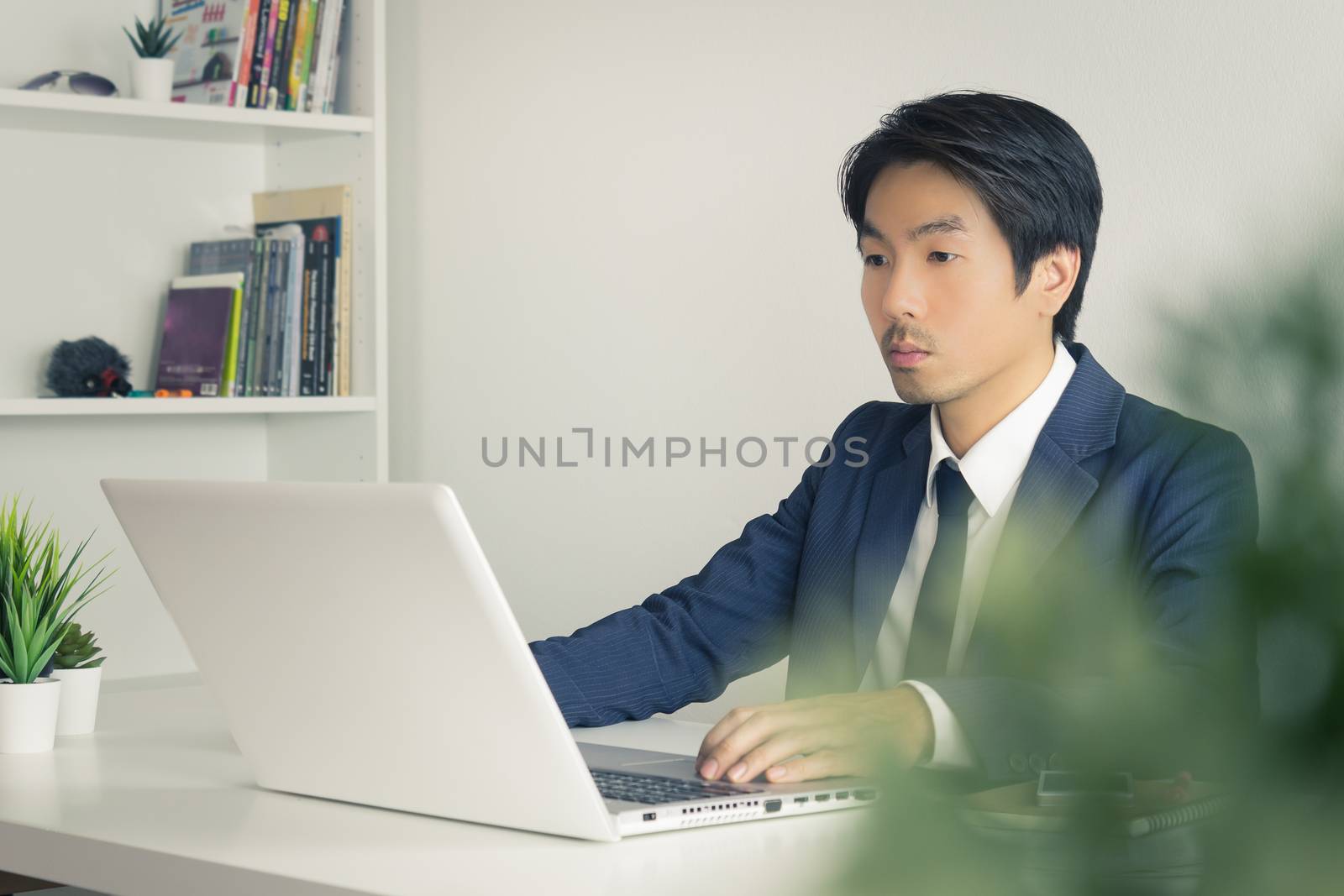 Asian Businessman In front of Laptop Monitor and Tree Foreground. Asian businessman working in office