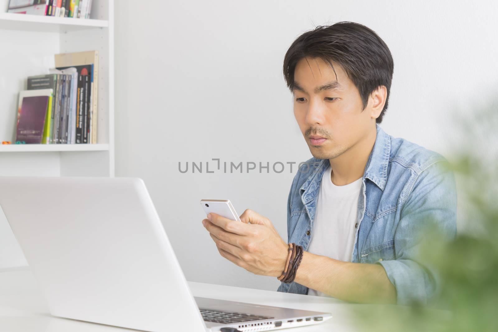 Young Asian Casual Businessman Send Messages to Colleague at Workplace in Home Office. Casual business or informal business in home office