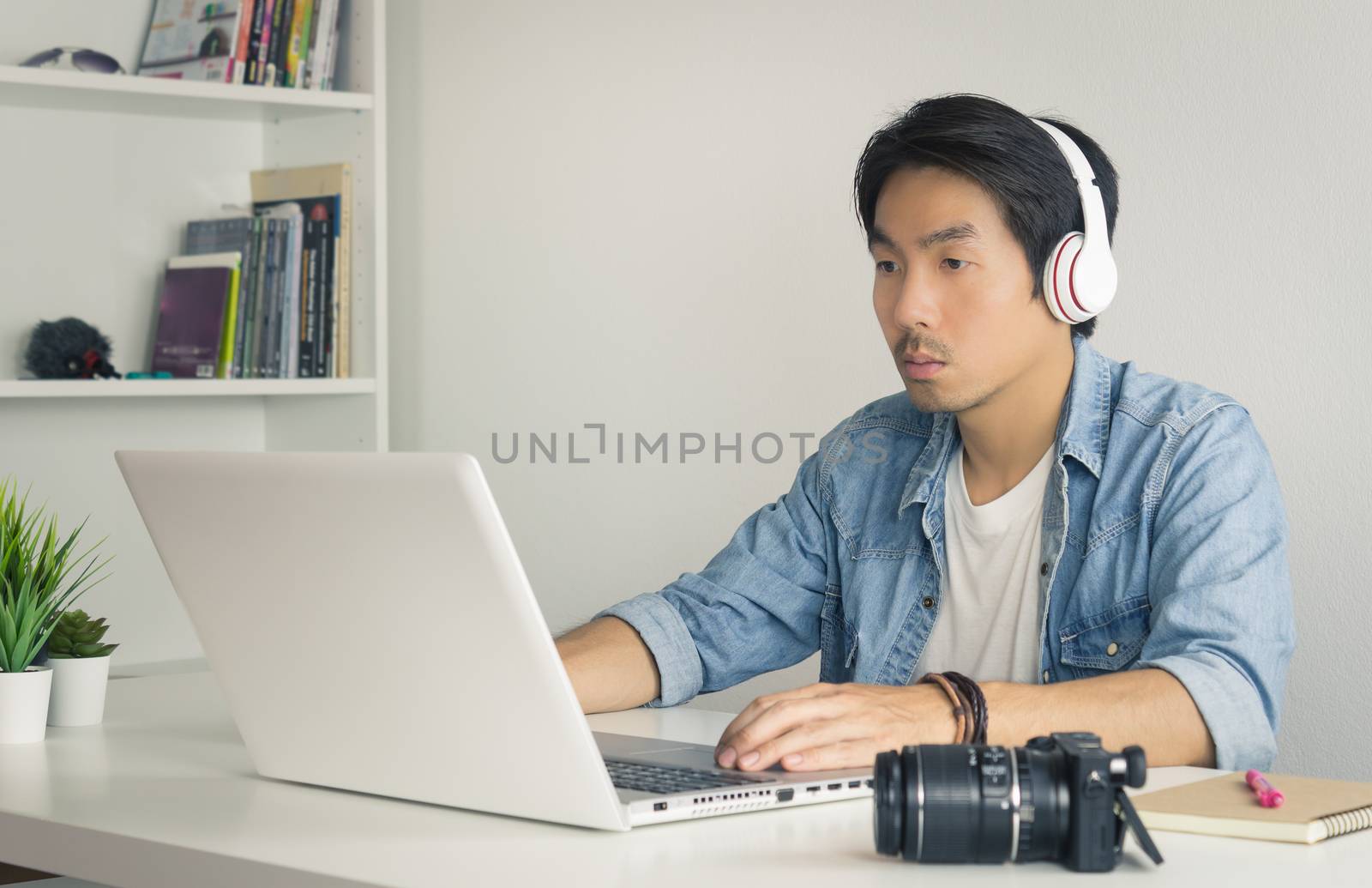 Asian Freelance Videographer in Denim or Jeans Shirt Checking Multimedia Sound by Laptop in Home Office. Freelance Videographer working with technology
