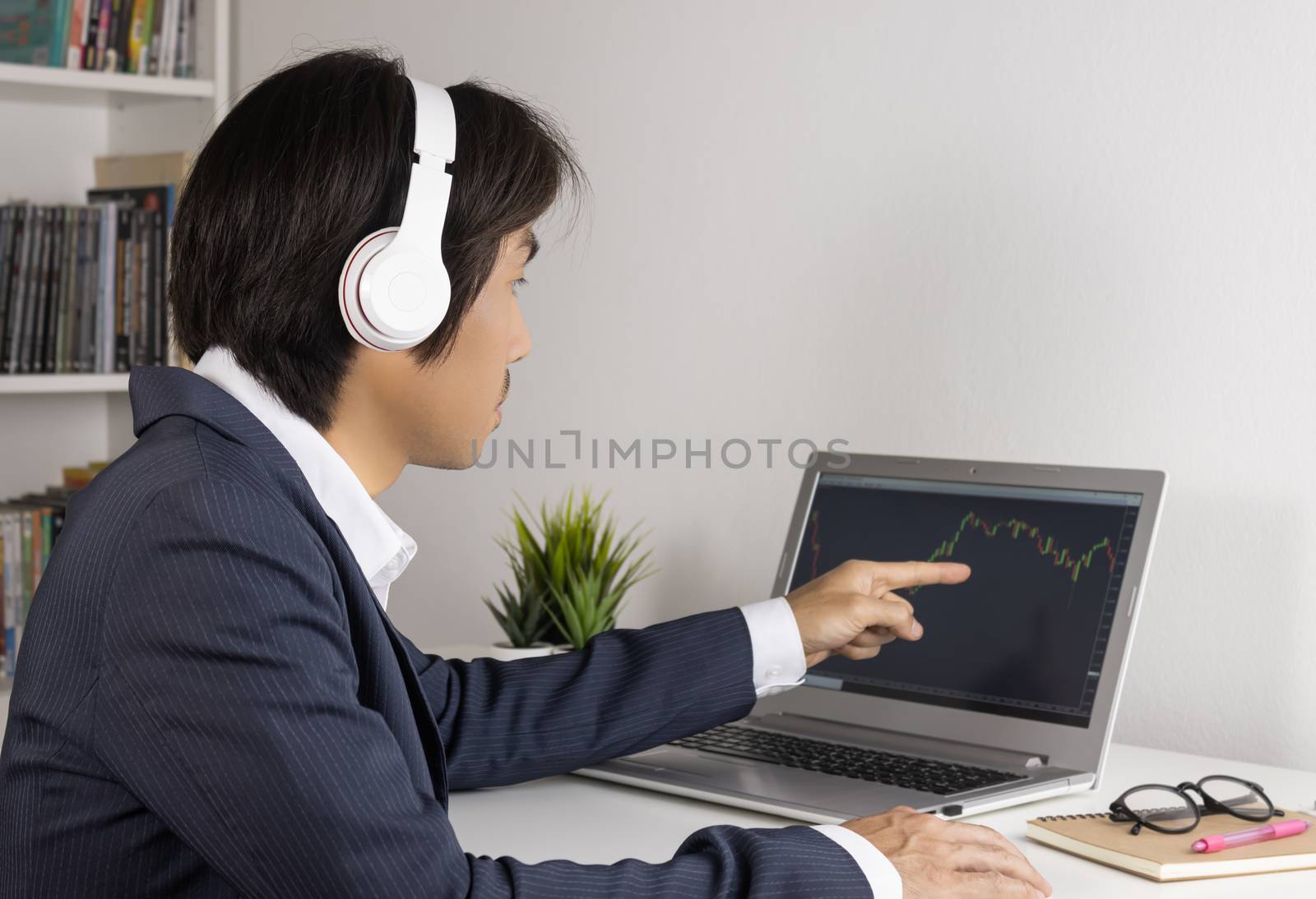 Young Asian Forex Trader or Investor or Businessman in Suit Trading and Pointing Forex or Stock Chart in Laptop Monitor in Trader Room