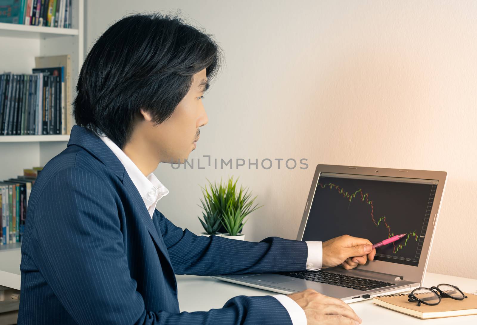 Young Asian Forex Trader or Investor or Businessman in Suit Trading and Pointing Forex or Stock Chart on Laptop Screen in Trader Room in Vintage Tone