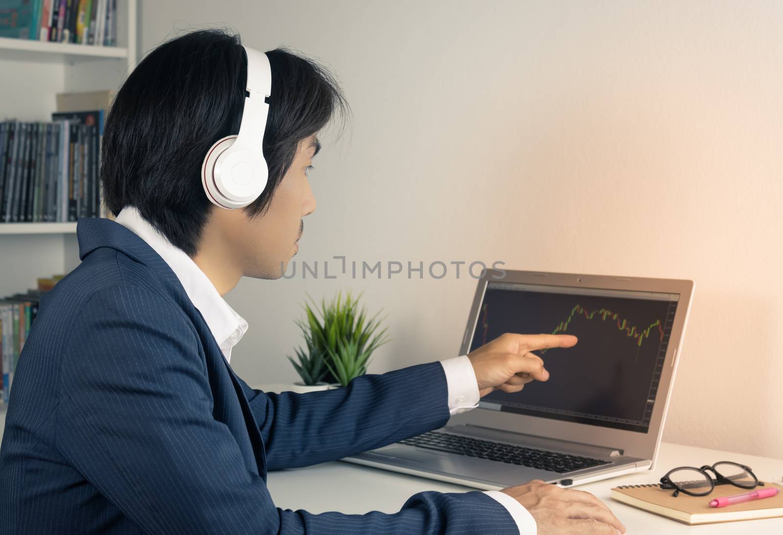 Young Asian Forex Trader or Investor or Businessman in Suit Trading and Pointing Forex or Stock Chart in Laptop Monitor in Trader Room in Vintage Tone