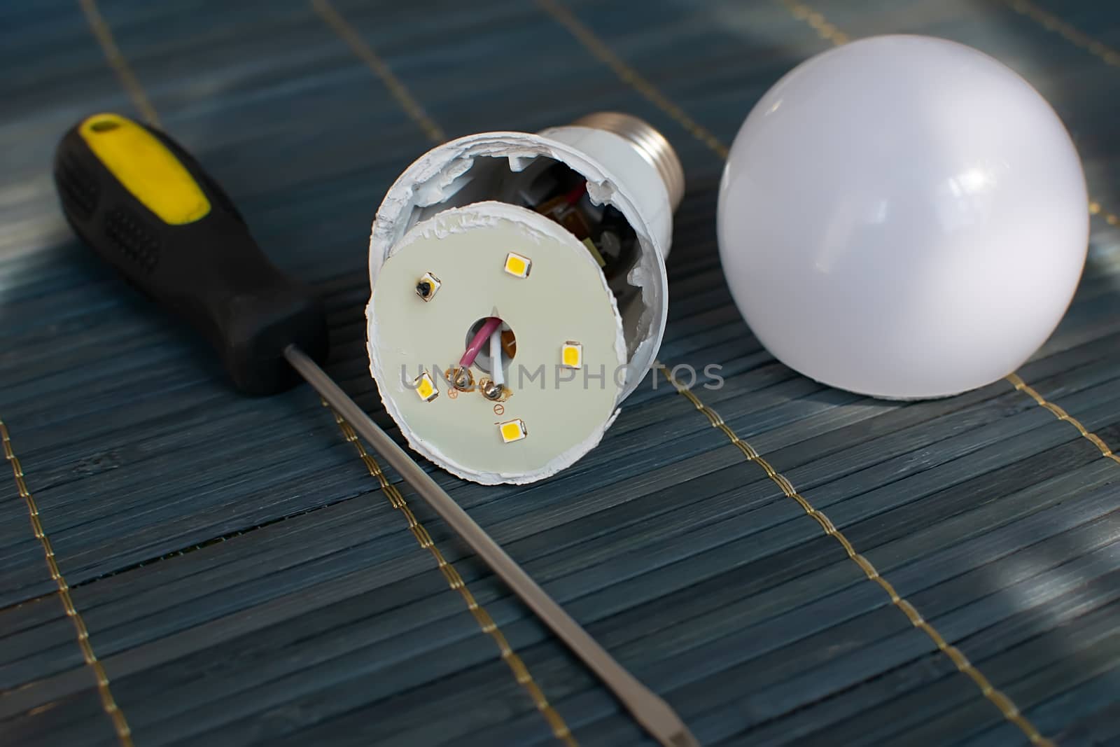 faulty, disassembled led household lamp with a burnt led element is on the table next to the screwdriver