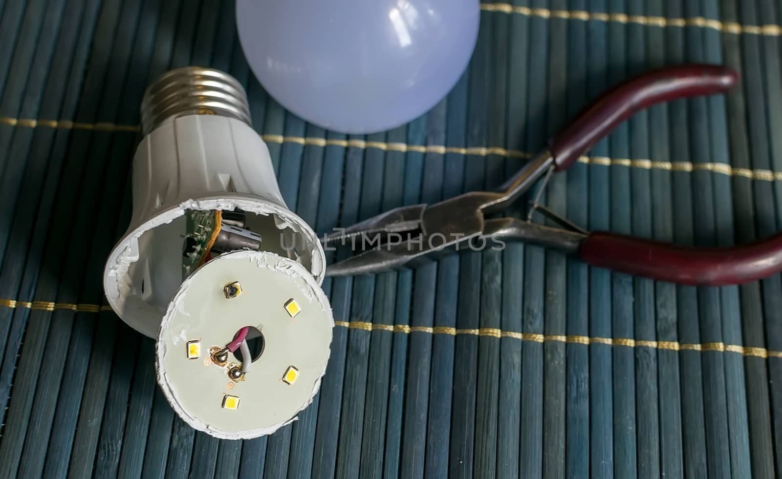 faulty, disassembled led household lamp with a burnt led element is on the table next to the pliers