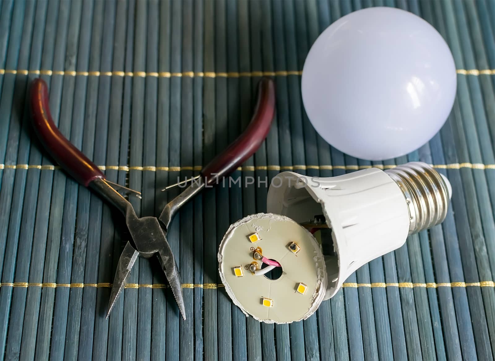 faulty, disassembled led household lamp with a burnt led element is on the table next to the pliers