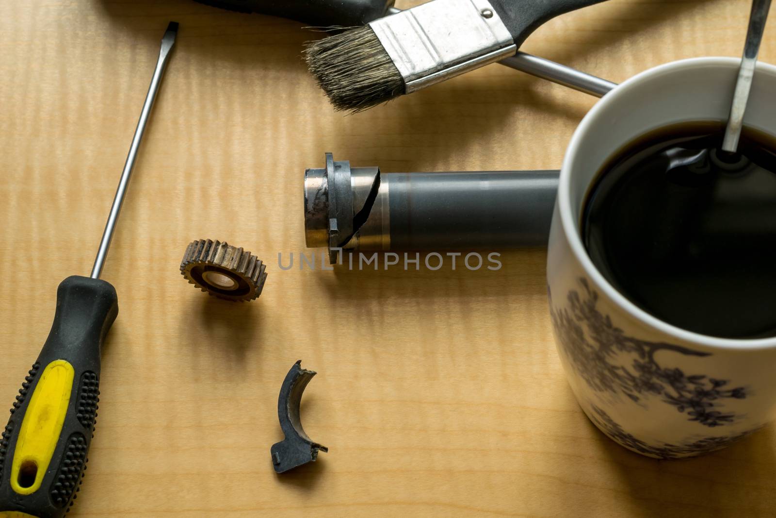 printer parts, tools, grease, broken gear and coffee mug on the table