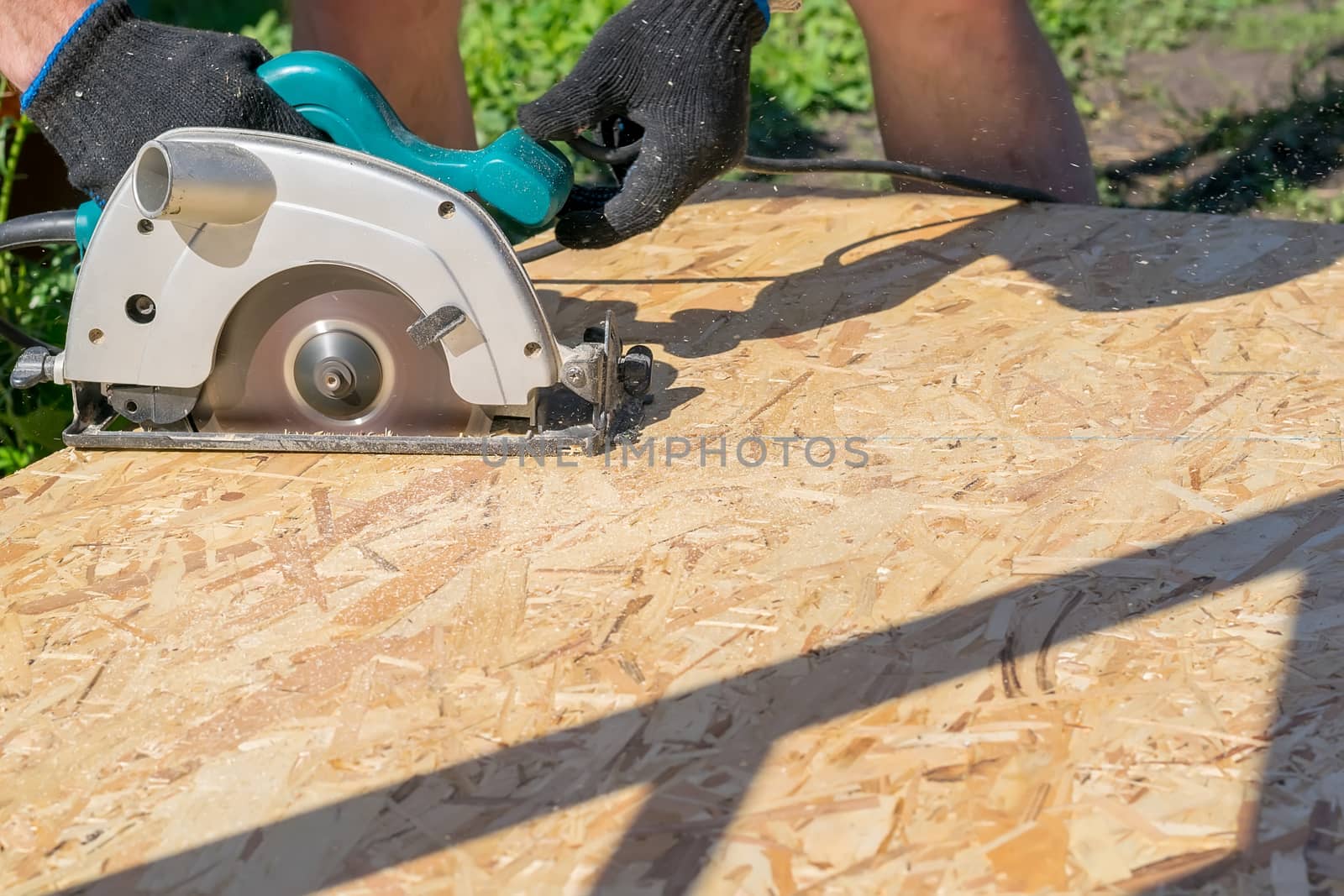 a man sawing a Board with a power tool, chips fly in all directions. Construction, wood processing