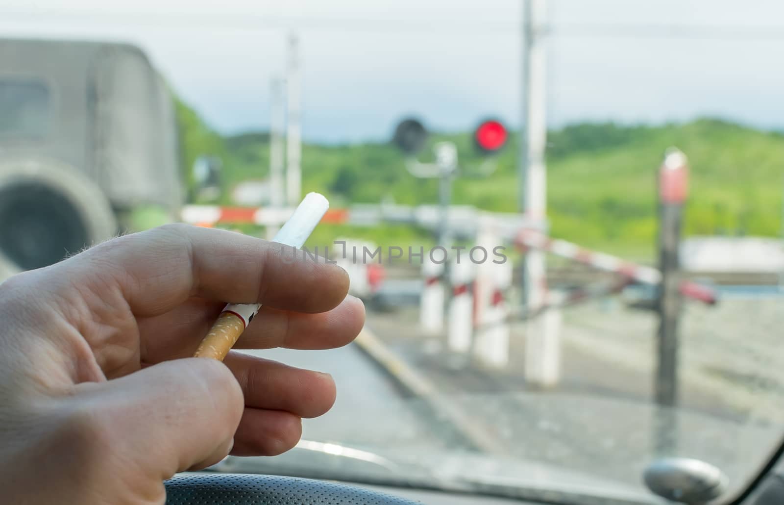 View of the driver hand with a cigarette on the steering wheel of the car, which stopped before a closed railway crossing at a red light by jk3030