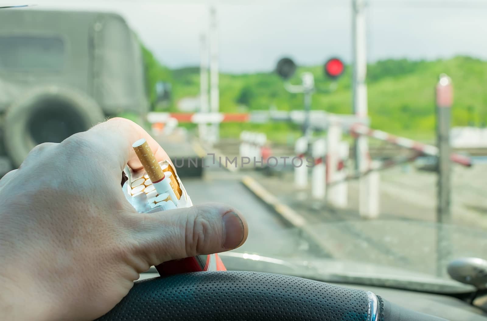 View of the driver hand with a pack of cigarettes on the steering wheel of the car, which stopped before a closed railway crossing at a red light by jk3030
