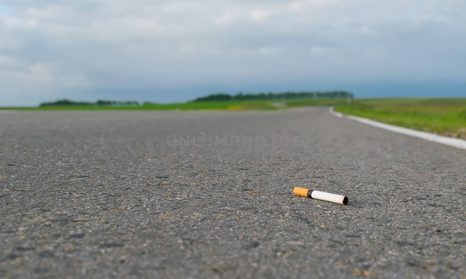 View of cigarette lying on the asphalt on a country road in the cloudy weather