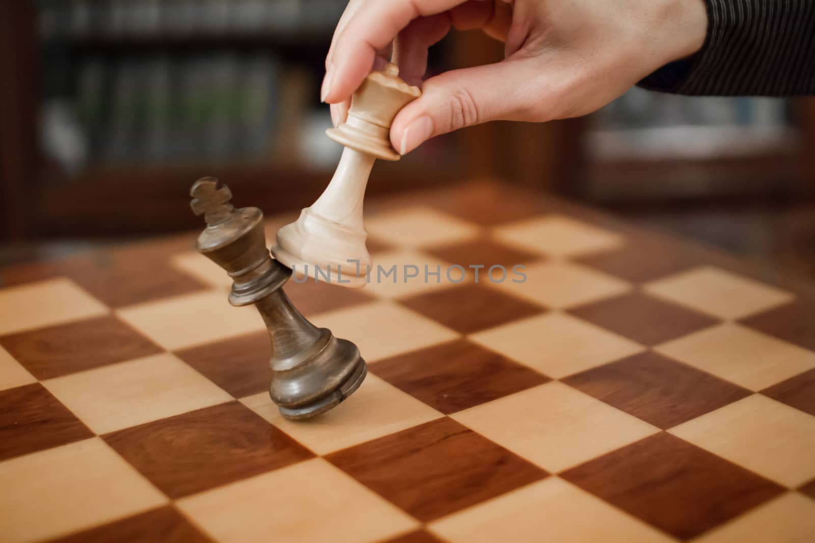 Concept: the woman who dominates the man. A woman's hand gives checkmate to the king with the queen on a wooden chessboard, with no other pieces in play