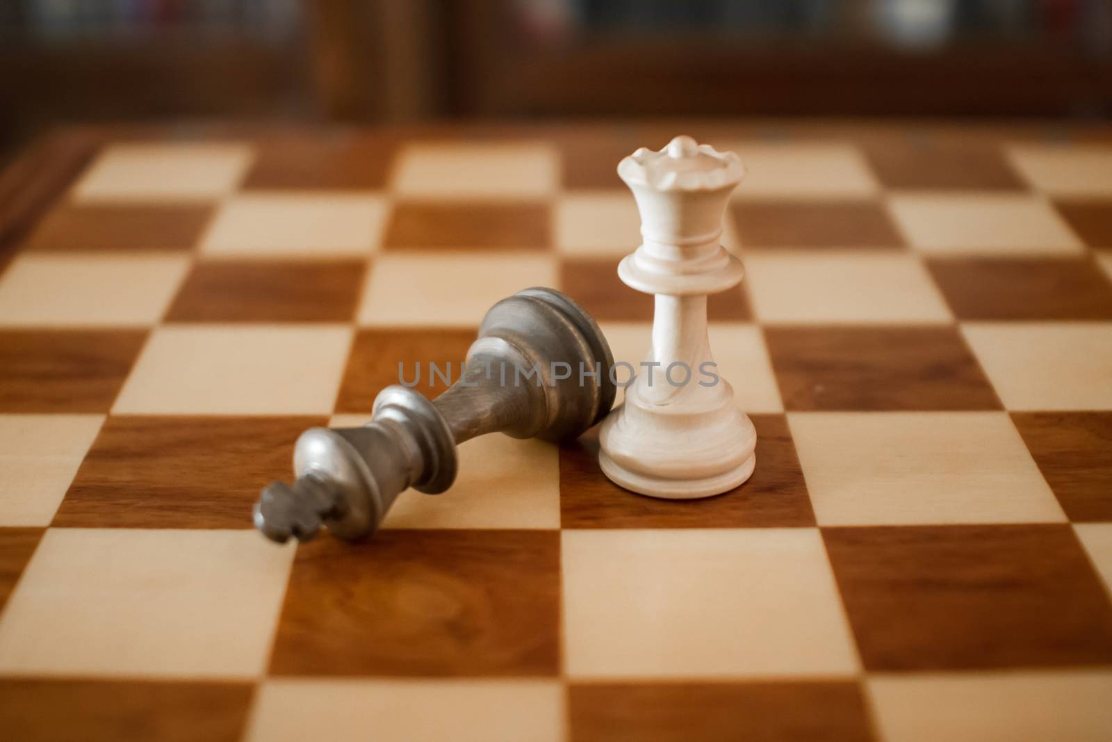 Concept: the woman who dominates the man. A wooden chess board with the king on the ground after the checkmate and the queen standing side by side without any other piece in play