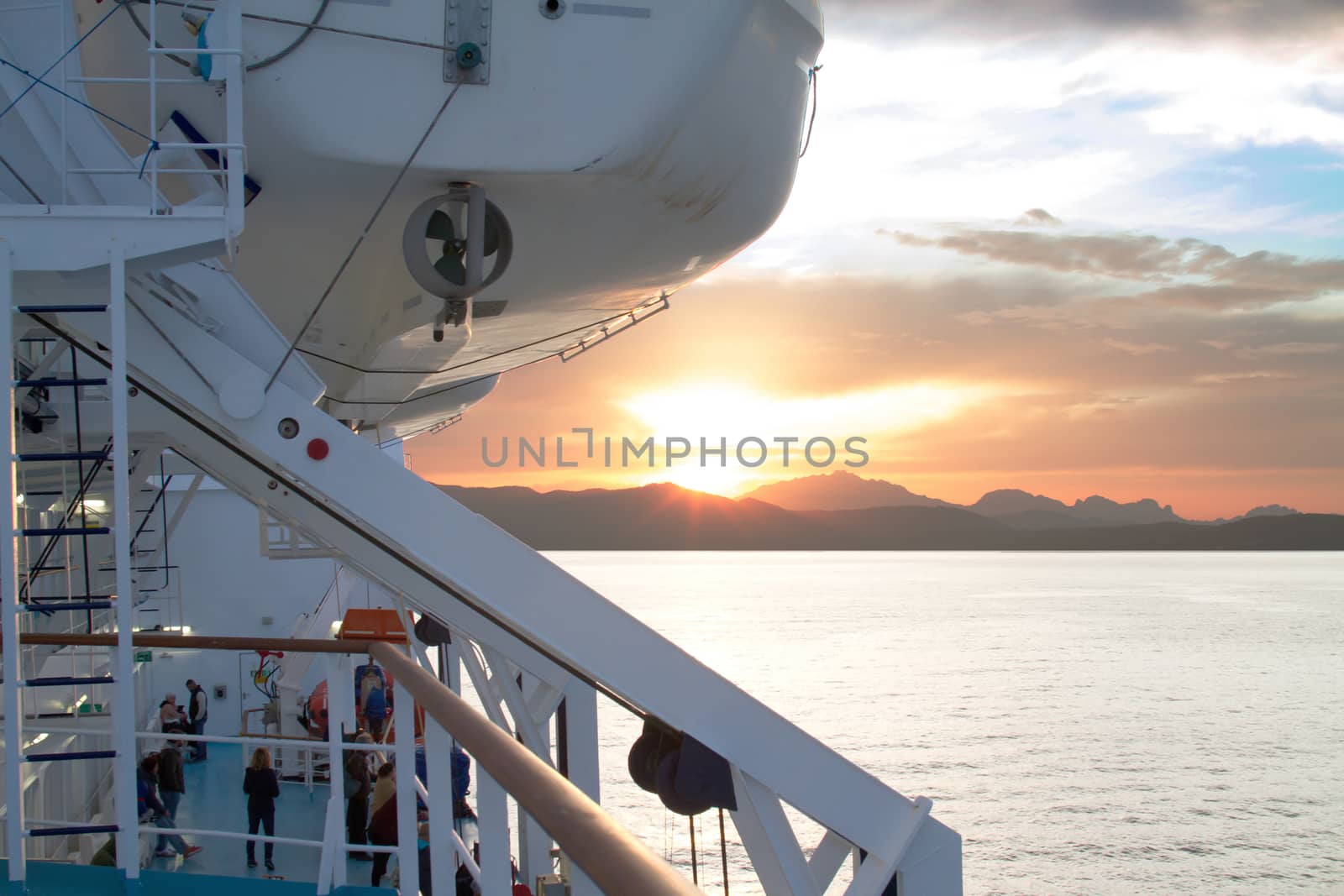 Sunrise on the Sardinian sea coast with intense orange color seen from the sea on the ferry that is about to dock and people on board
