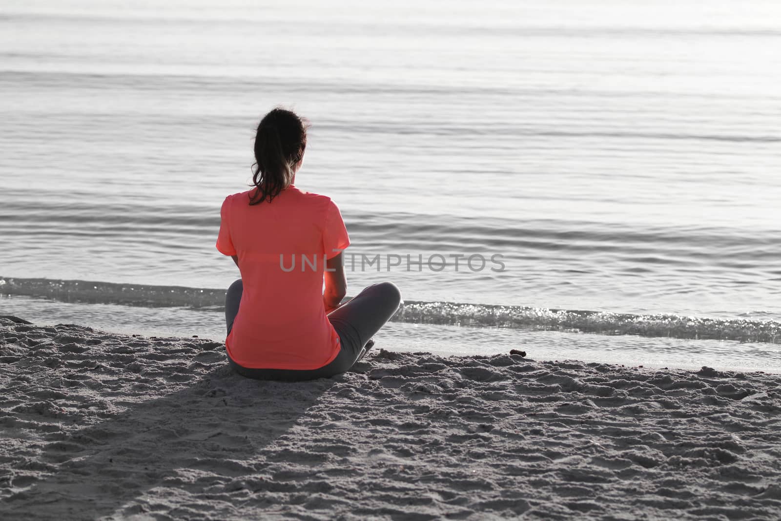 Young woman sitting on the shoreline of the sea at dawn in athle by robbyfontanesi