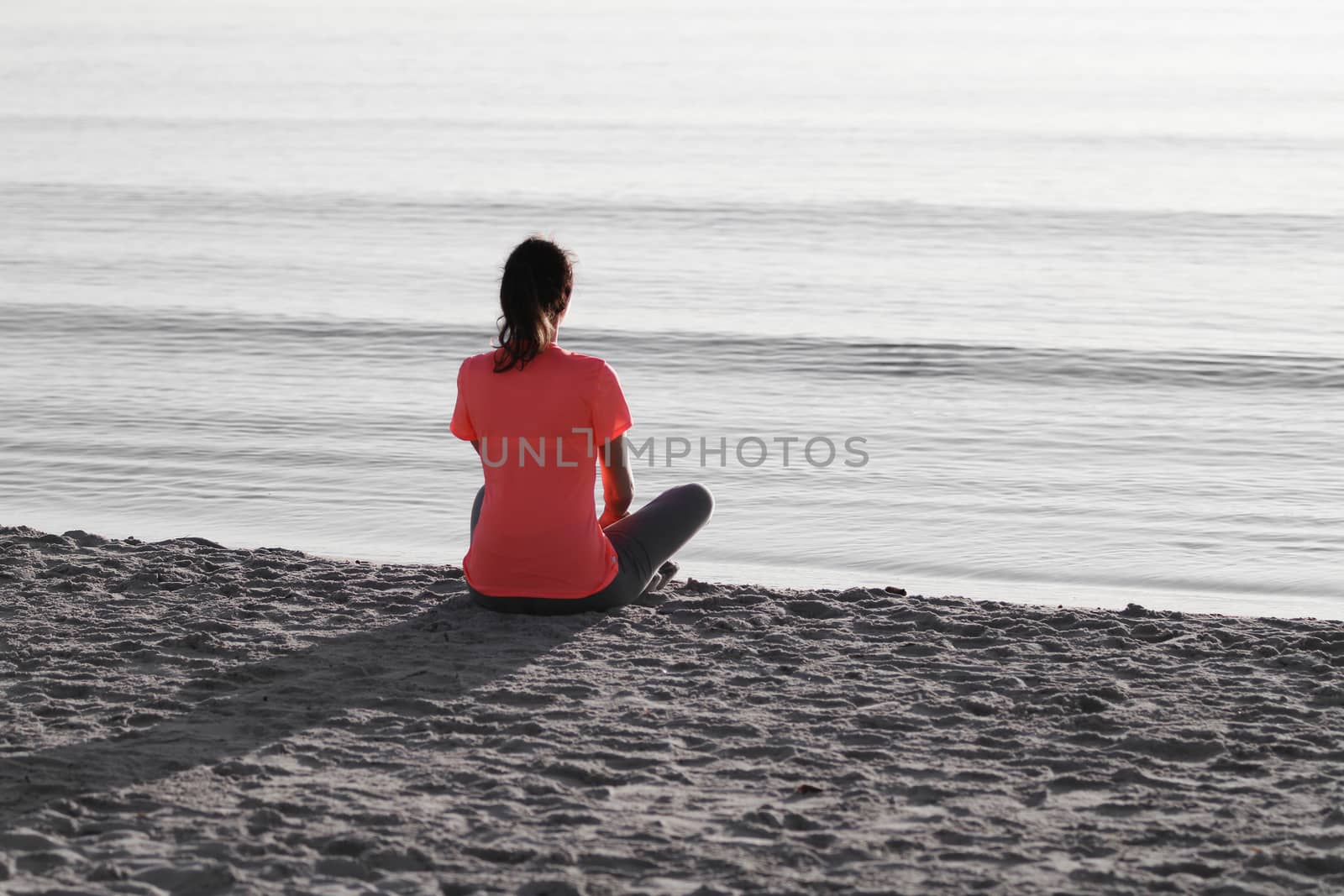 Young woman sitting on the shoreline of the sea at dawn in athle by robbyfontanesi